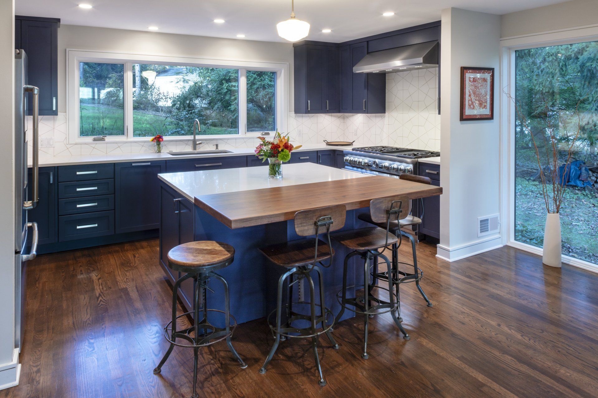 Modern kitchen with dark cabinets, wood floors, large island, and stools by a bright window