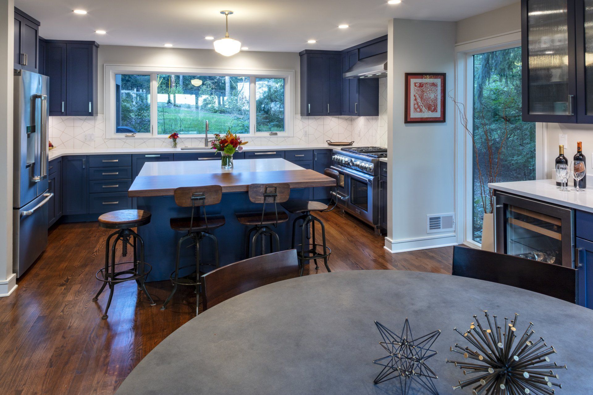 Modern kitchen with dark cabinets, large island, hardwood floors, and a window overlooking greenery