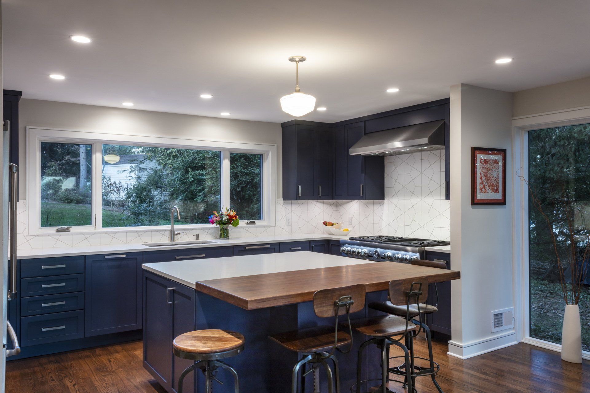 Modern kitchen with dark cabinets, white counters, large island, stools, and bright recessed lighting