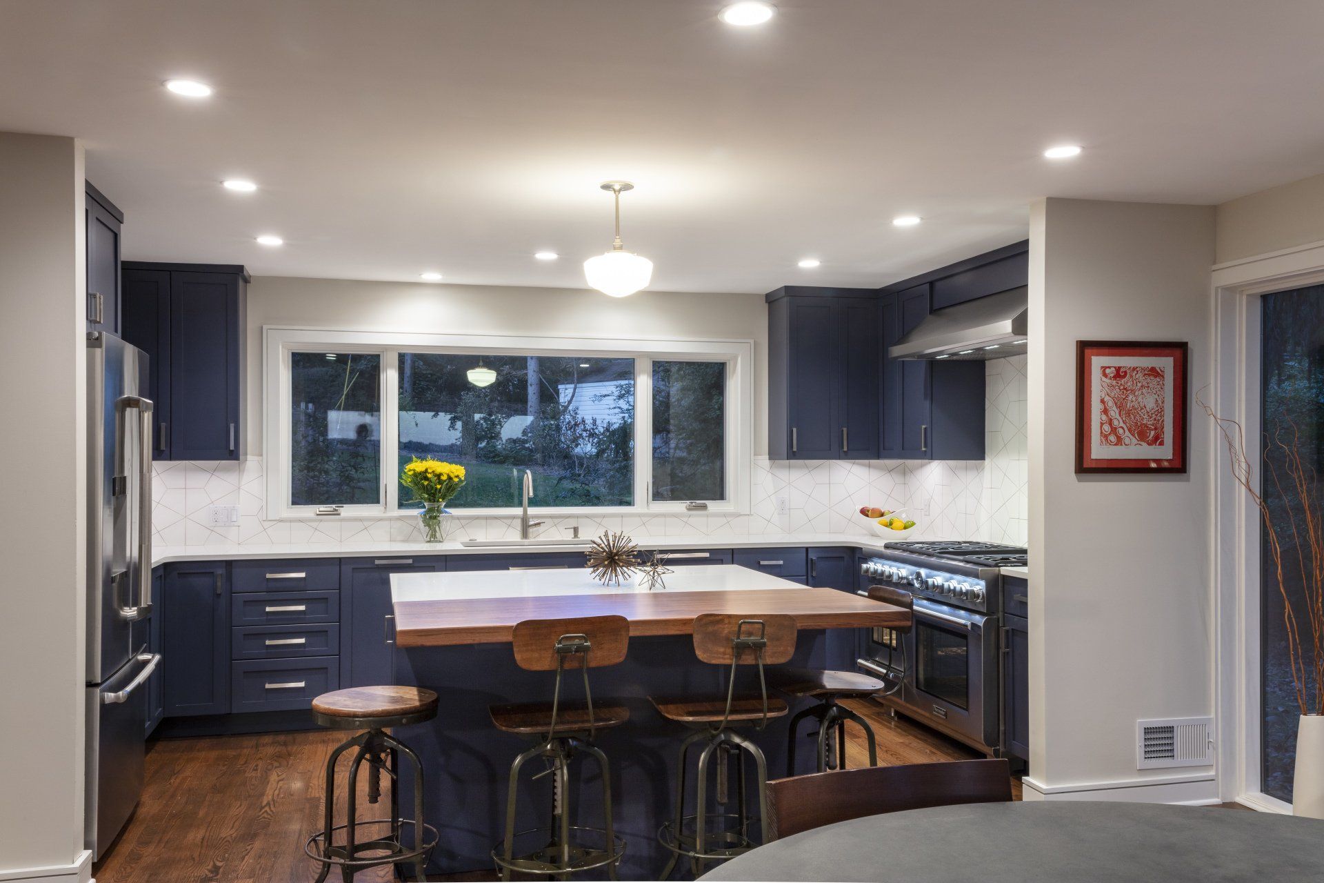 Modern kitchen with navy cabinets, island seating, white counters, and a large window over the sink