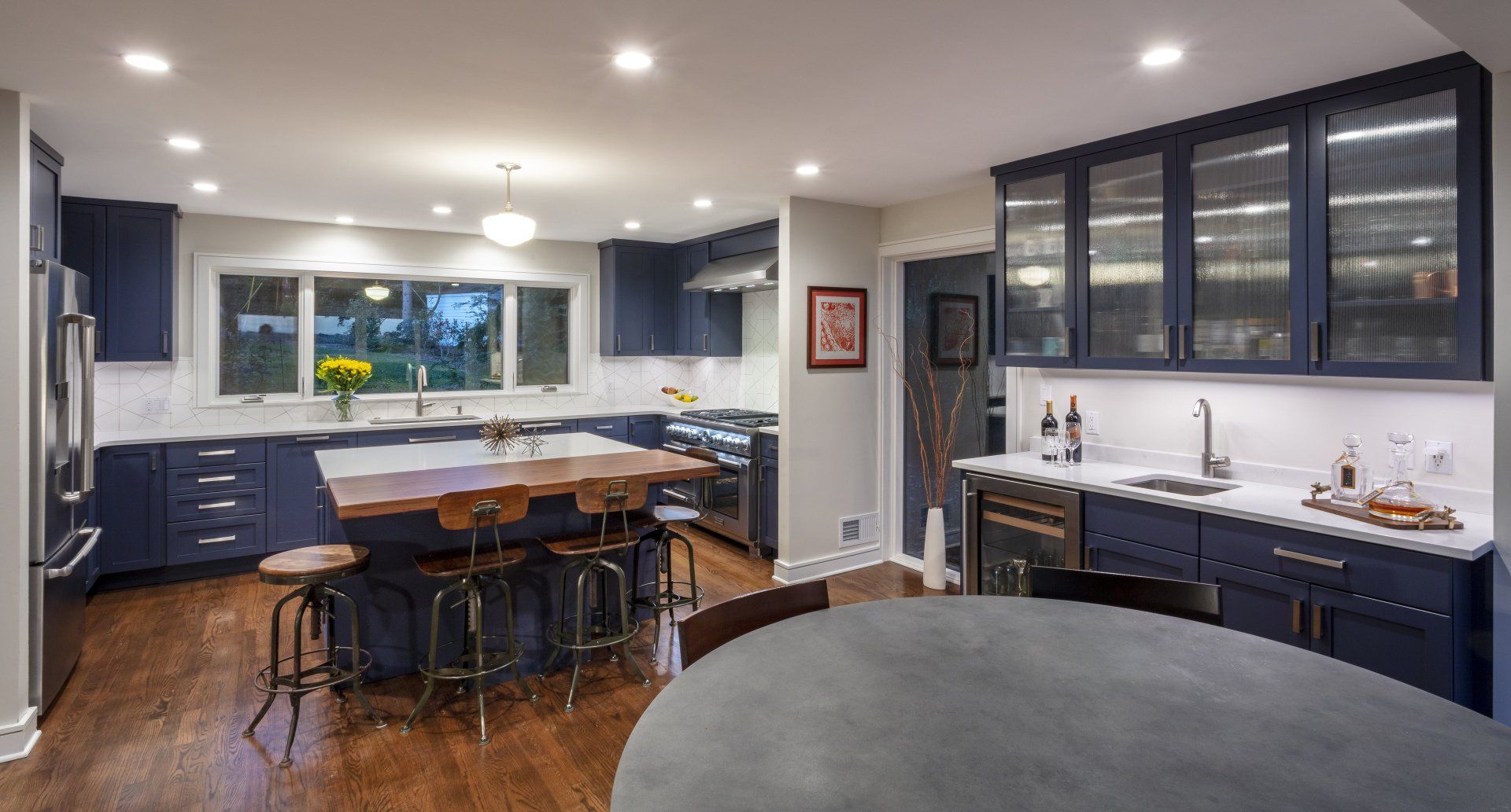 Modern kitchen with navy cabinets, large island, white countertops, and hardwood floors, lit by recessed lights