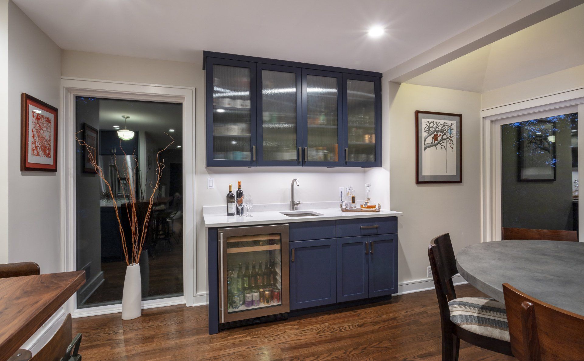 Modern kitchen with dark blue cabinets, wood floors, and a sink beneath glass-front upper cabinets