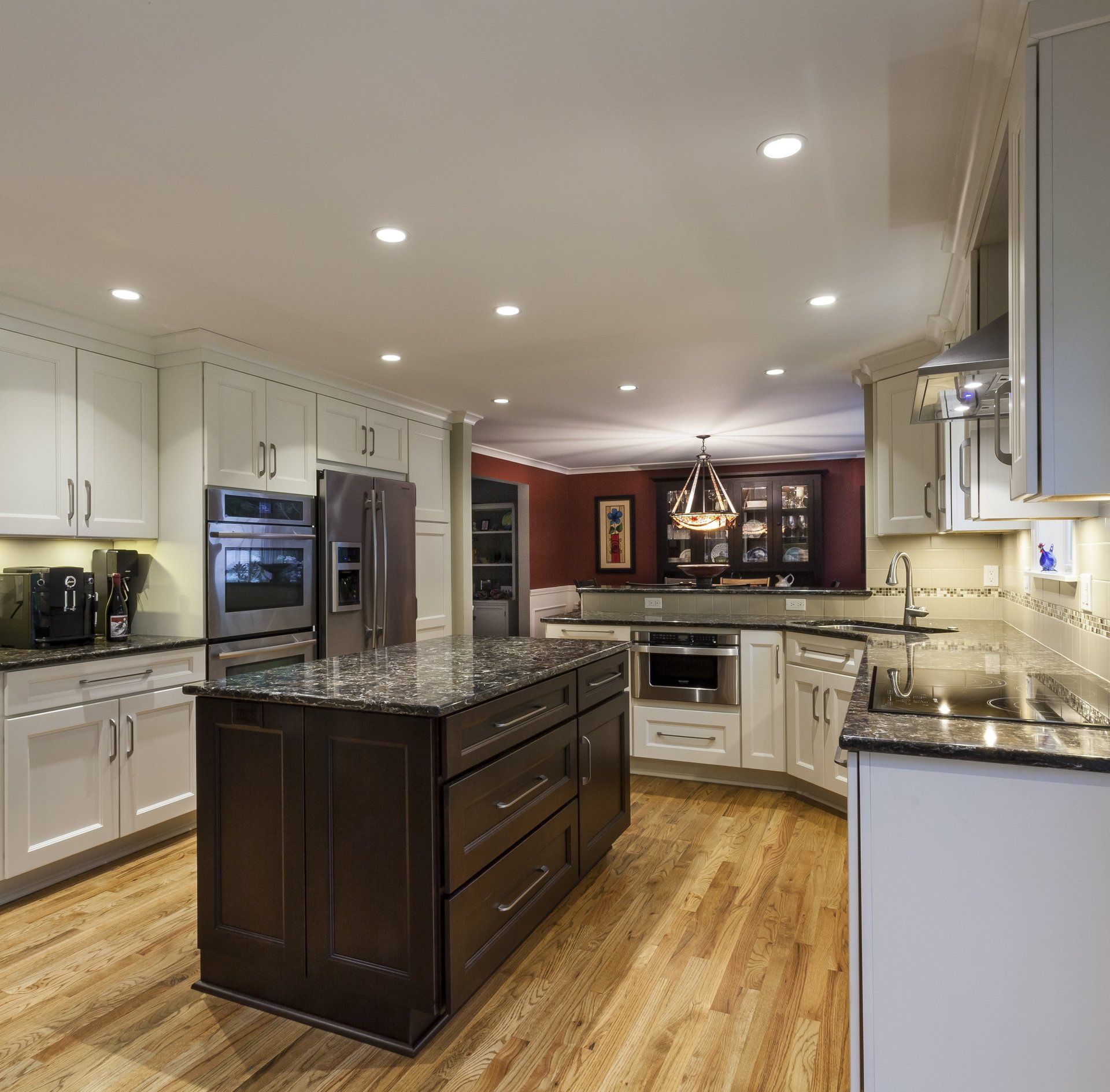 Modern kitchen with white cabinets, granite countertops, stainless appliances, and a dark island under recessed lighting