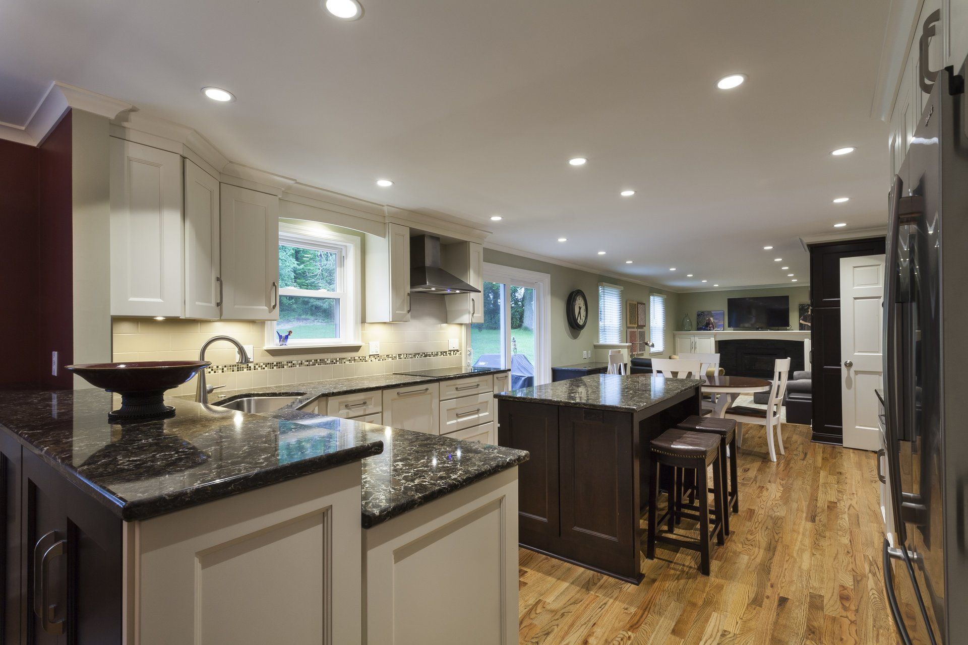 Spacious modern kitchen with white cabinets, granite counters, island seating, and hardwood floors