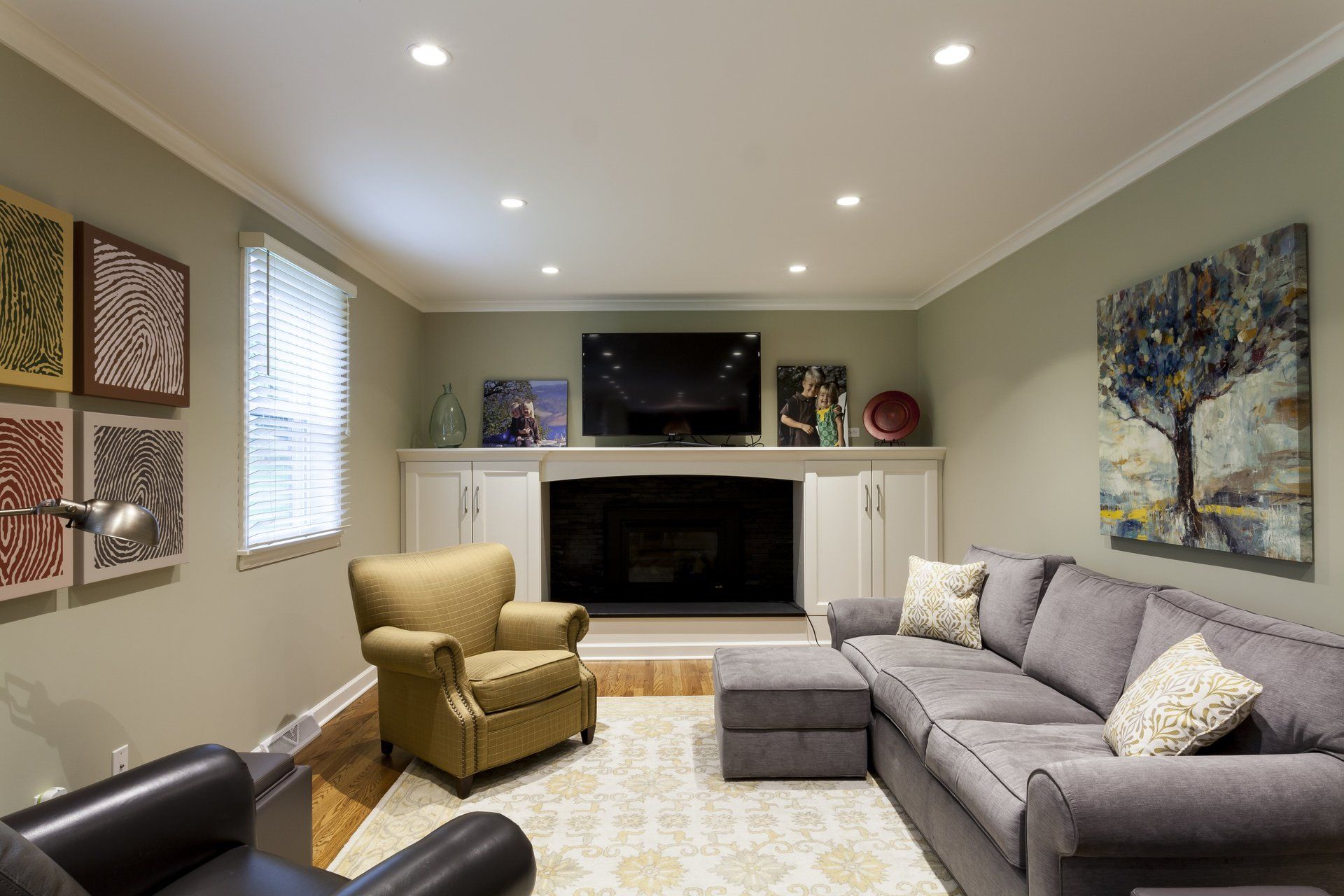 Living room with gray sectional, armchair, fireplace, wall art, and recessed ceiling lights