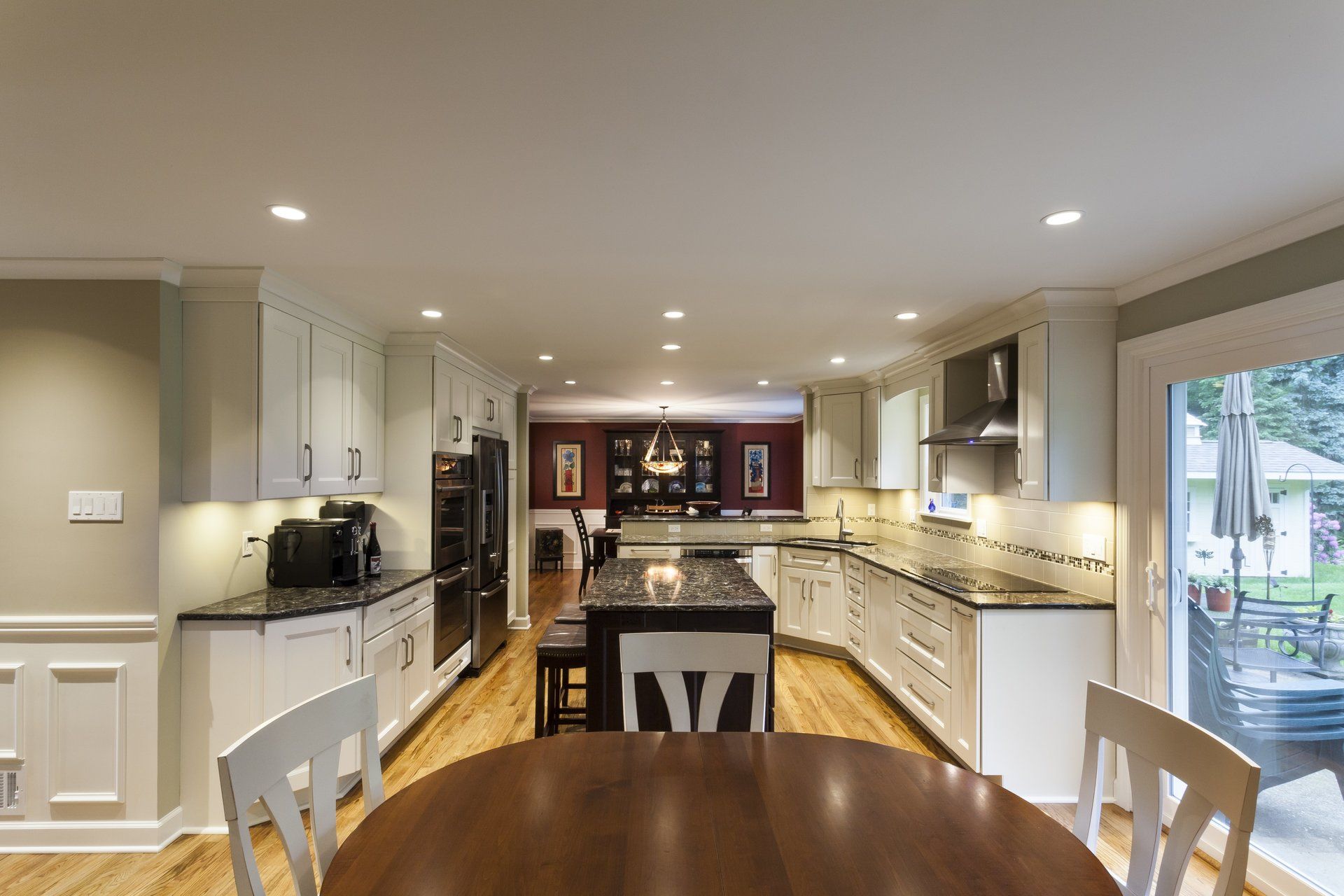Bright kitchen with white cabinets, granite island, and dining table, opening to a patio through sliding glass doors