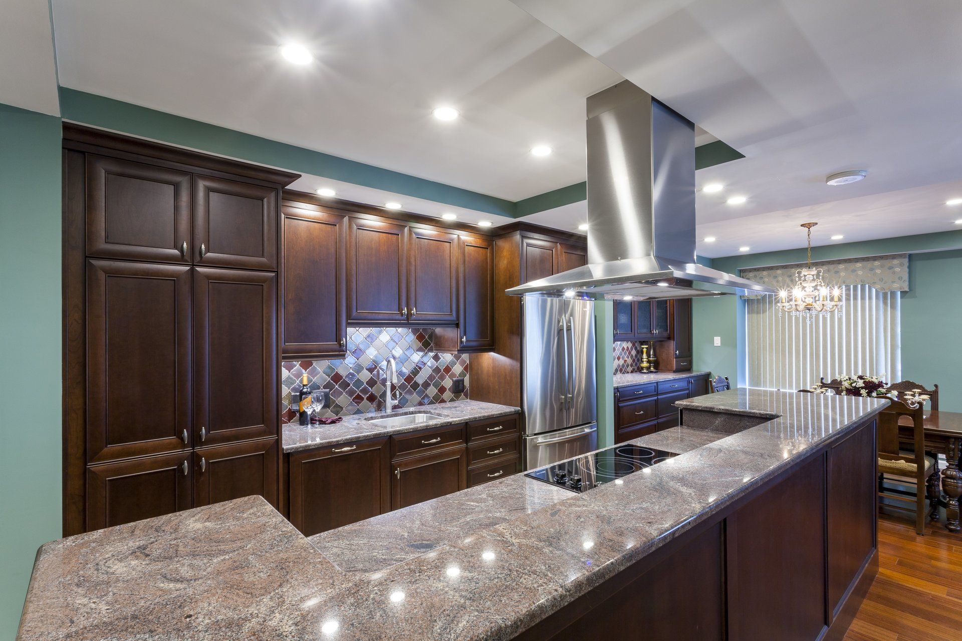 Modern kitchen with dark wood cabinets, granite island, stainless hood, and recessed lighting
