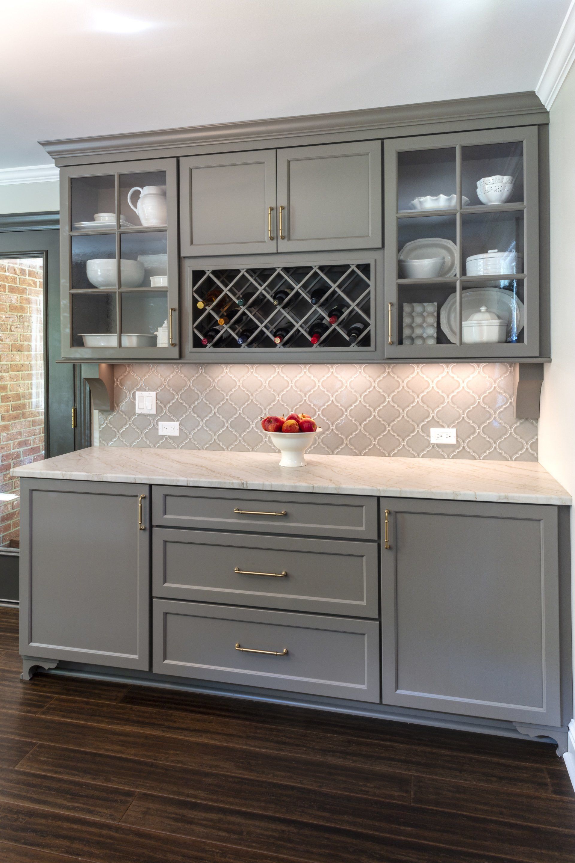 Gray kitchen cabinets with glass fronts, wine rack, and marble-look countertop against a tiled backsplash