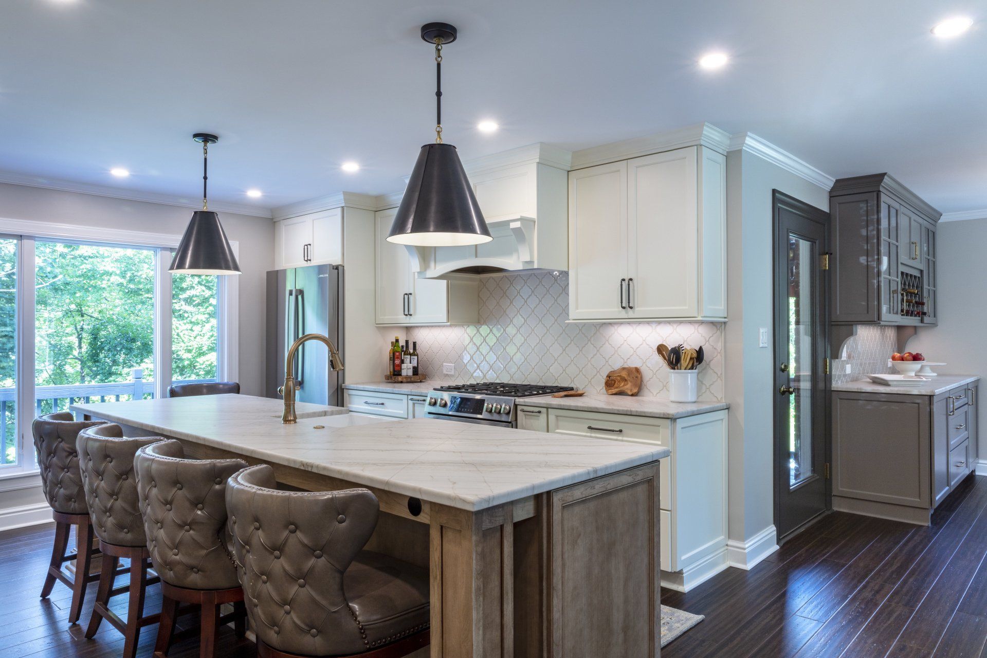Bright modern kitchen with white cabinets, marble island, pendant lights, and dark hardwood floors