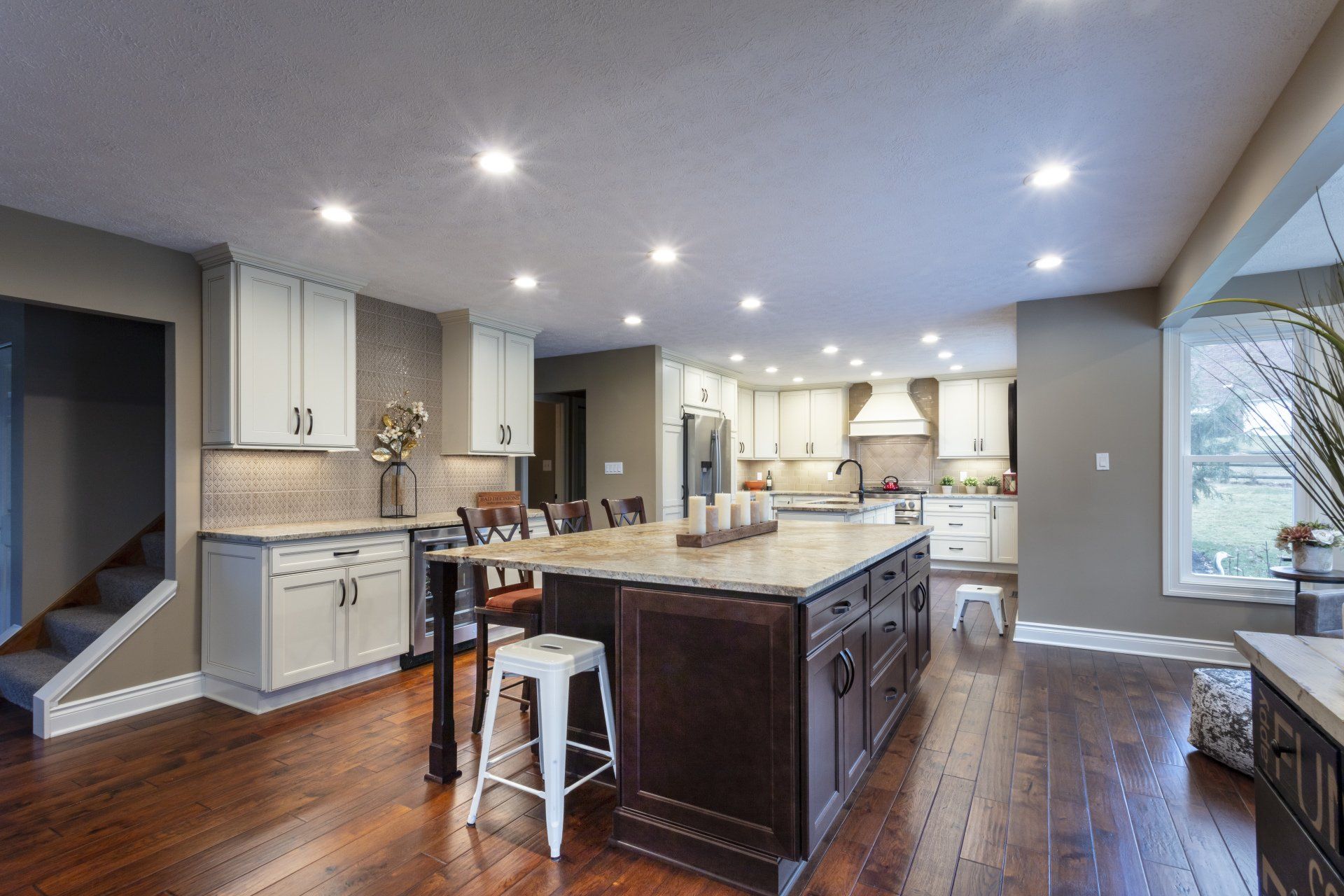 Modern open-plan kitchen with dark wood island, white cabinets, recessed lights, and a large window