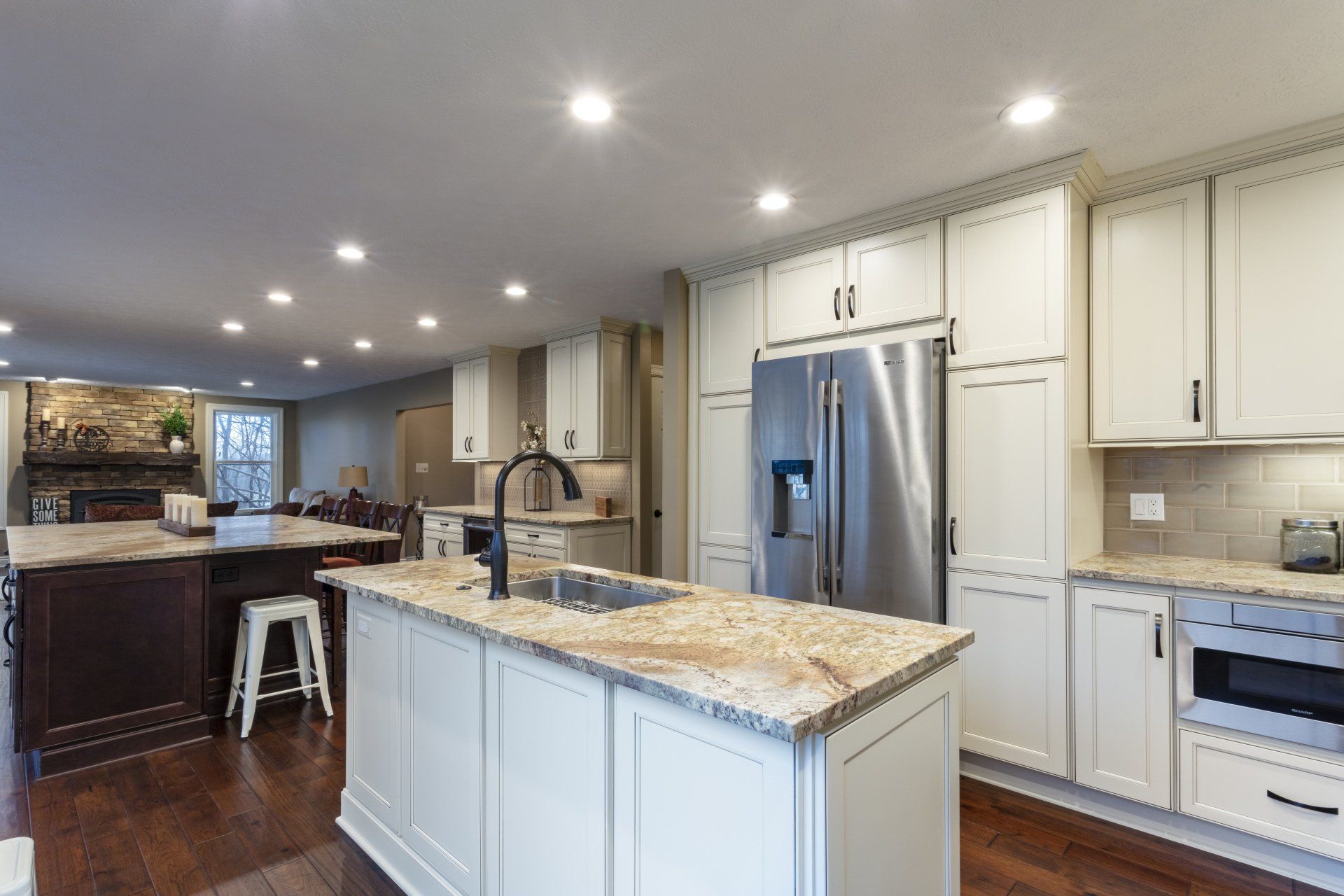Modern kitchen with white cabinets, granite island, stainless fridge, and recessed ceiling lights.