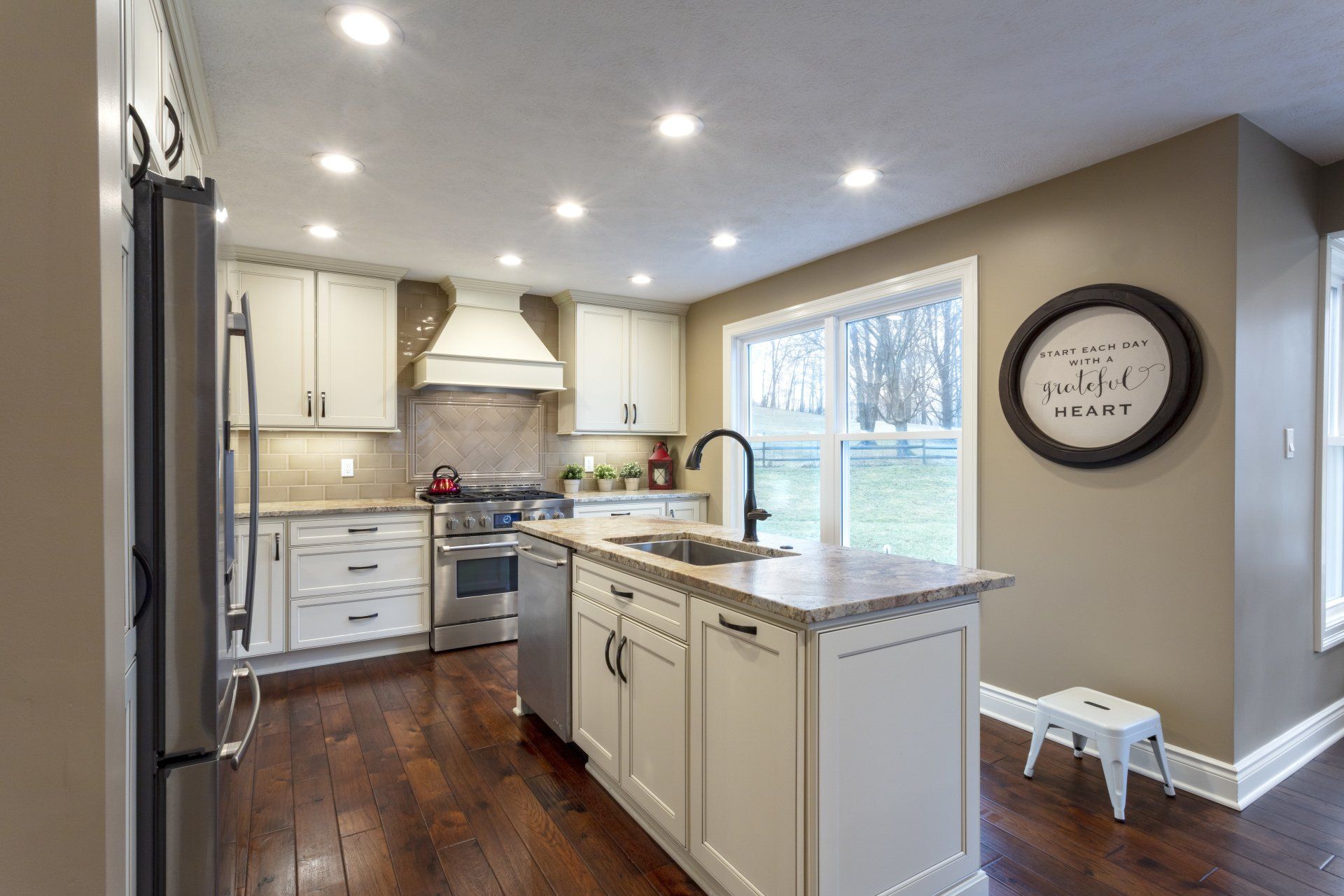 Bright kitchen with white cabinets, granite island, hardwood floors, and a large window.