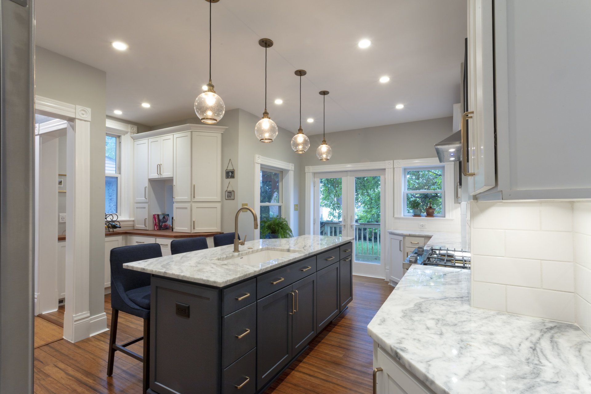 Bright modern kitchen with gray island, marble countertops, pendant lights, and hardwood floors
