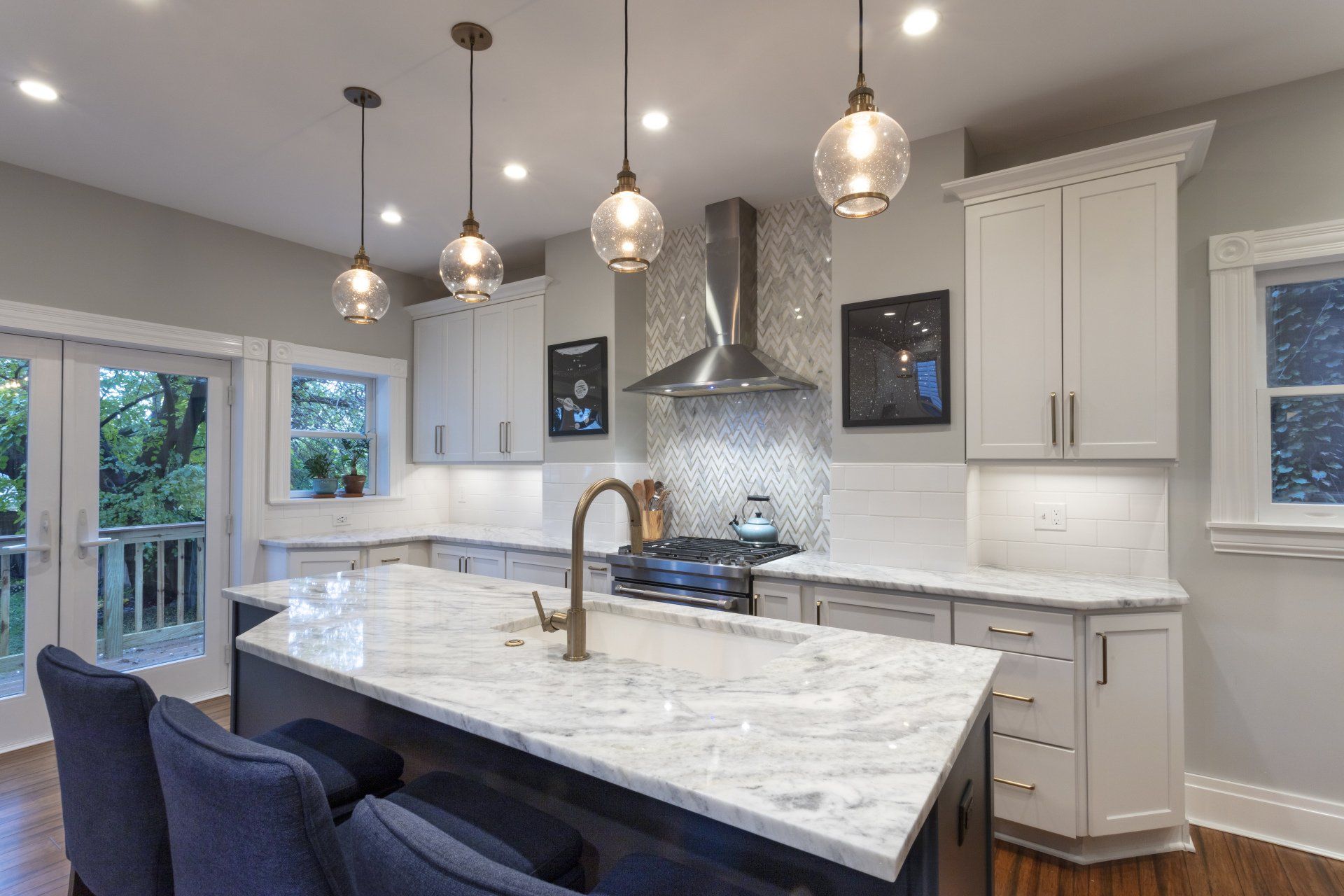 Modern kitchen with white cabinets, marble island, pendant lights, and stainless steel range hood