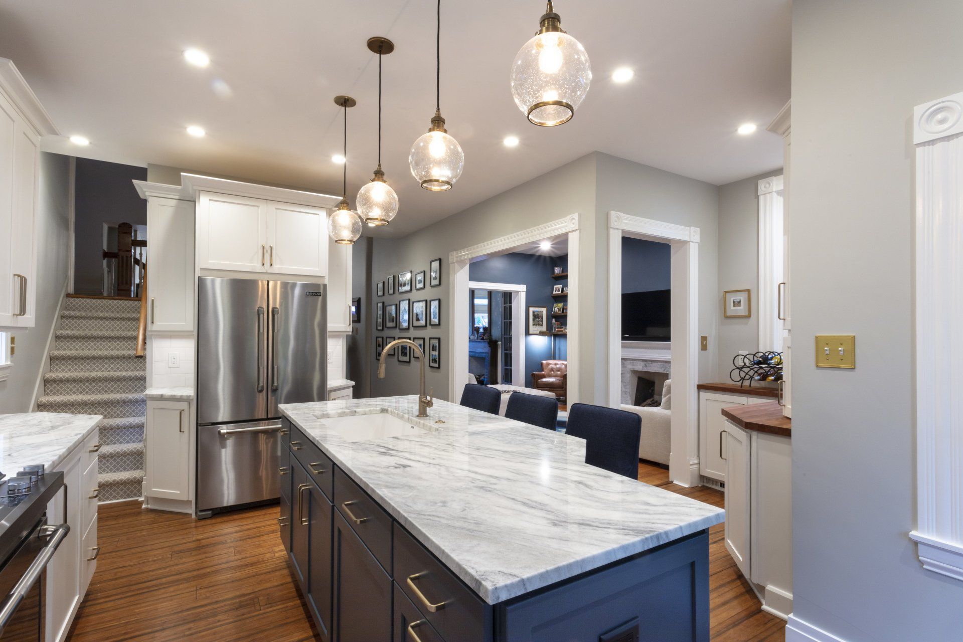 Modern kitchen with marble island, stainless-steel appliances, pendant lights, and hardwood floors