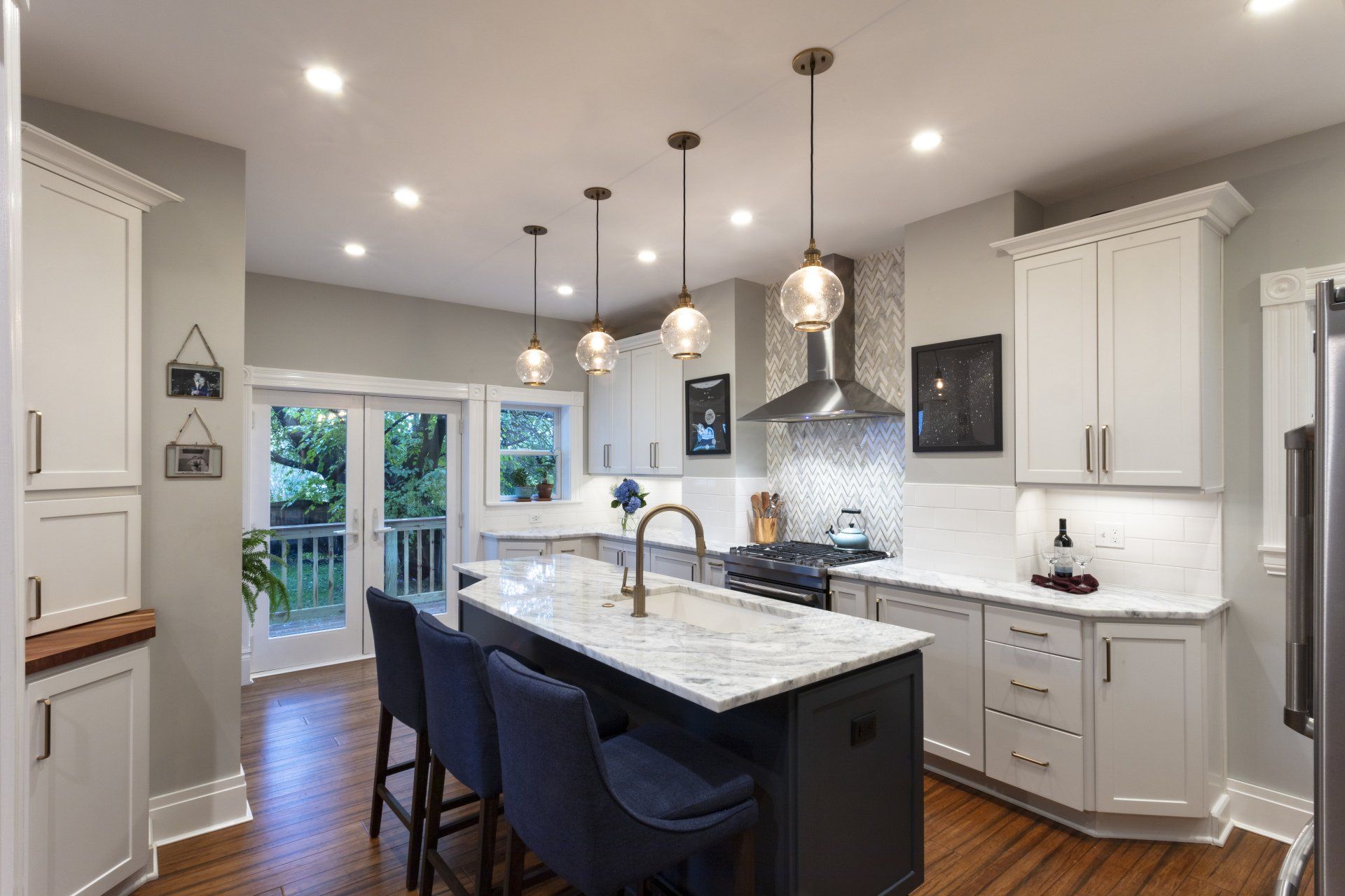 Bright modern kitchen with white cabinets, marble island, pendant lights, and patio doors.