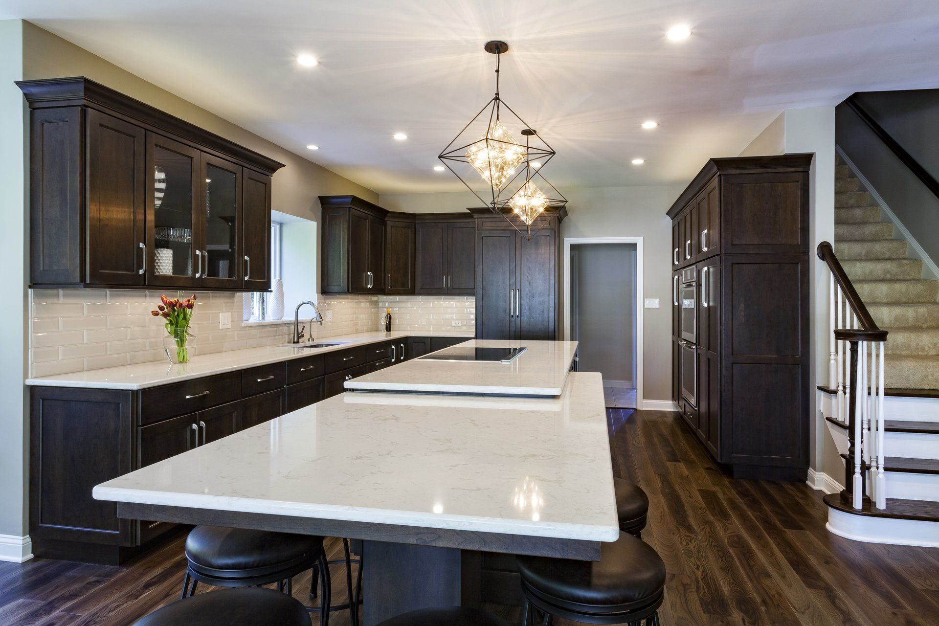 Modern kitchen with dark cabinets, white island, pendant light, and staircase on the right
