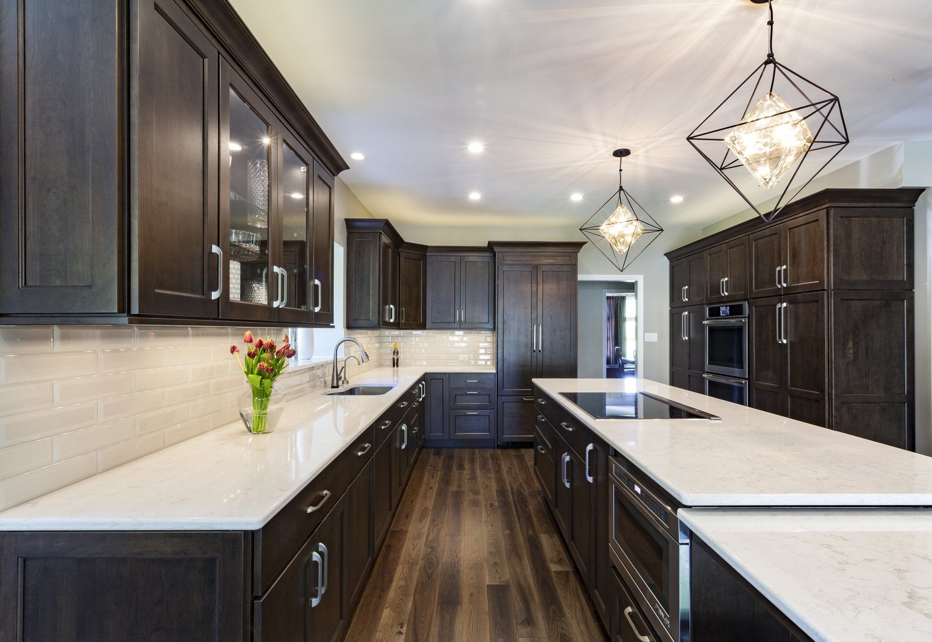 Modern kitchen with dark wood cabinets, white countertops, stainless appliances, and pendant lights.