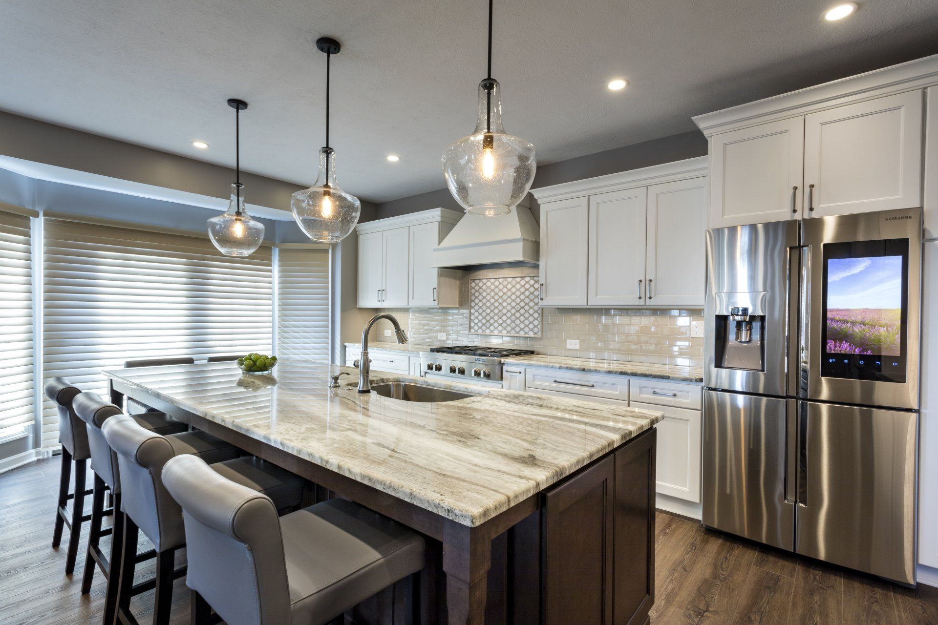 Modern kitchen with large island, pendant lights, barstools, stainless steel appliances, and white cabinets