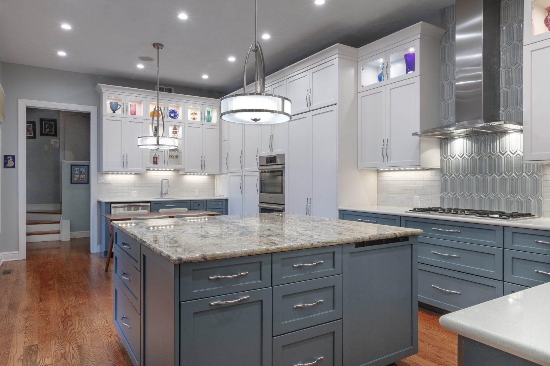 Bright modern kitchen with white cabinets, gray island, granite countertops, and hardwood floors