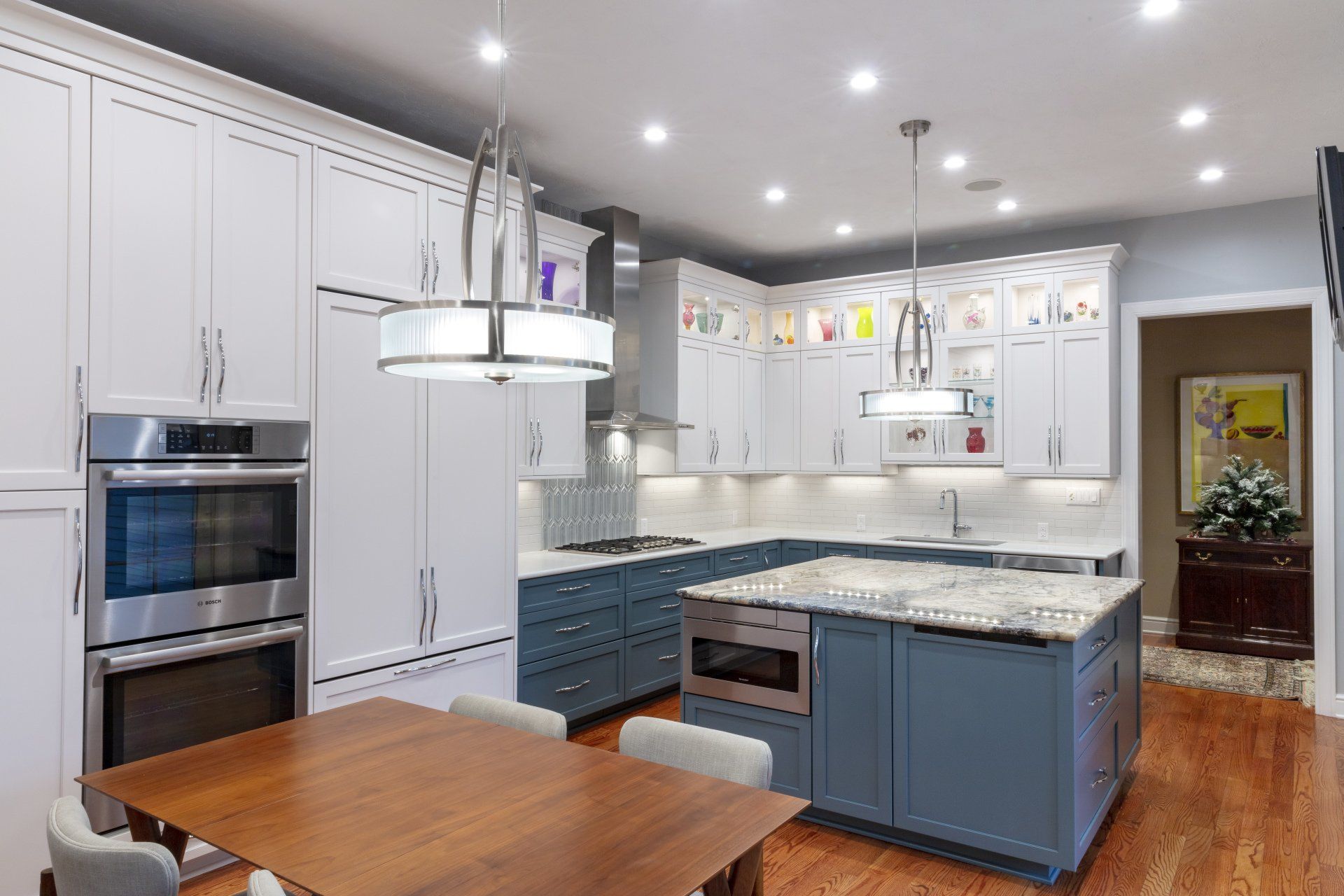 Bright modern kitchen with white and blue cabinets, island, wooden table, and recessed ceiling lights