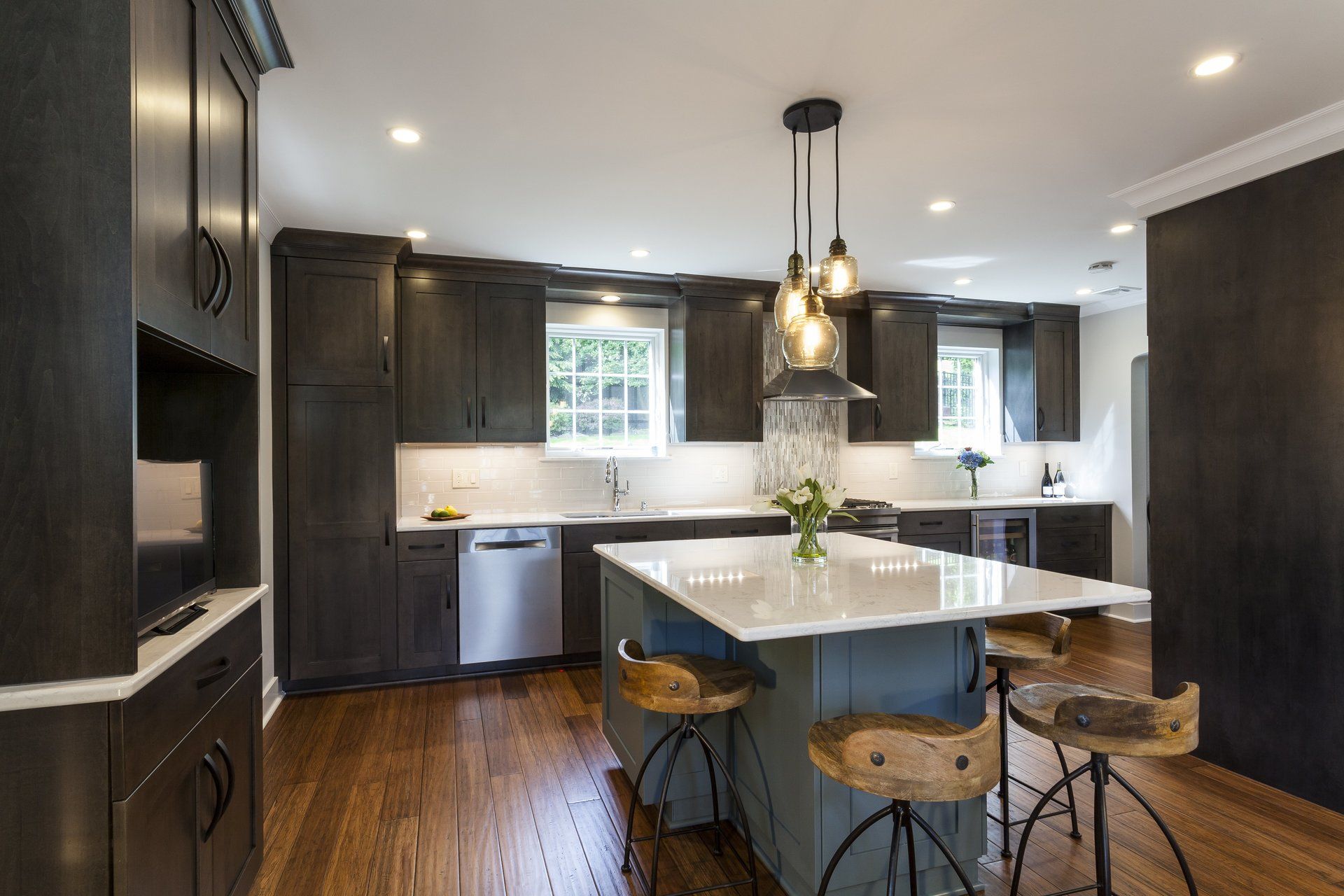 Modern kitchen with dark cabinets, white island, pendant lights, and wooden floors