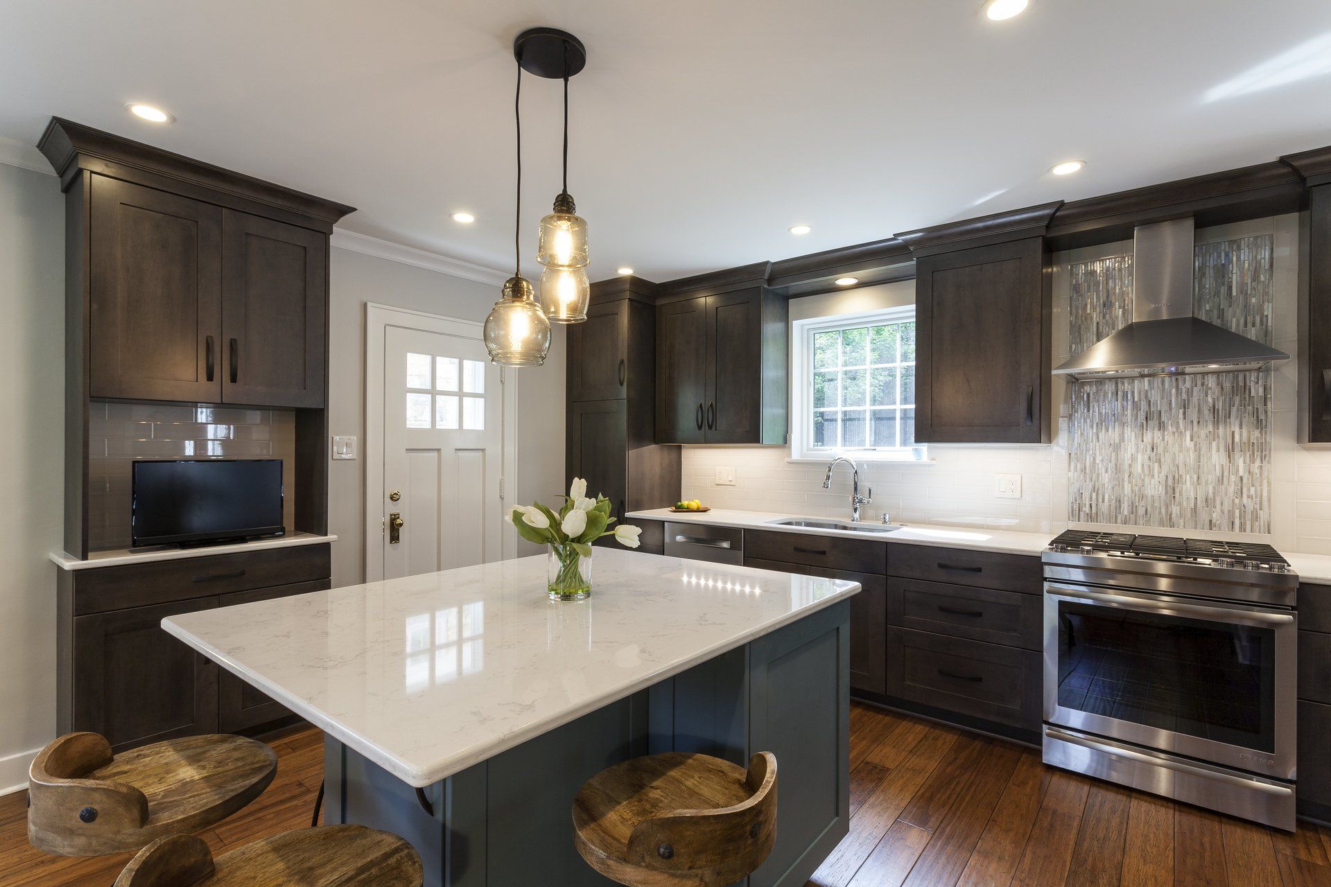 Modern kitchen with dark wood cabinets, white island, pendant lights, and stainless steel appliances