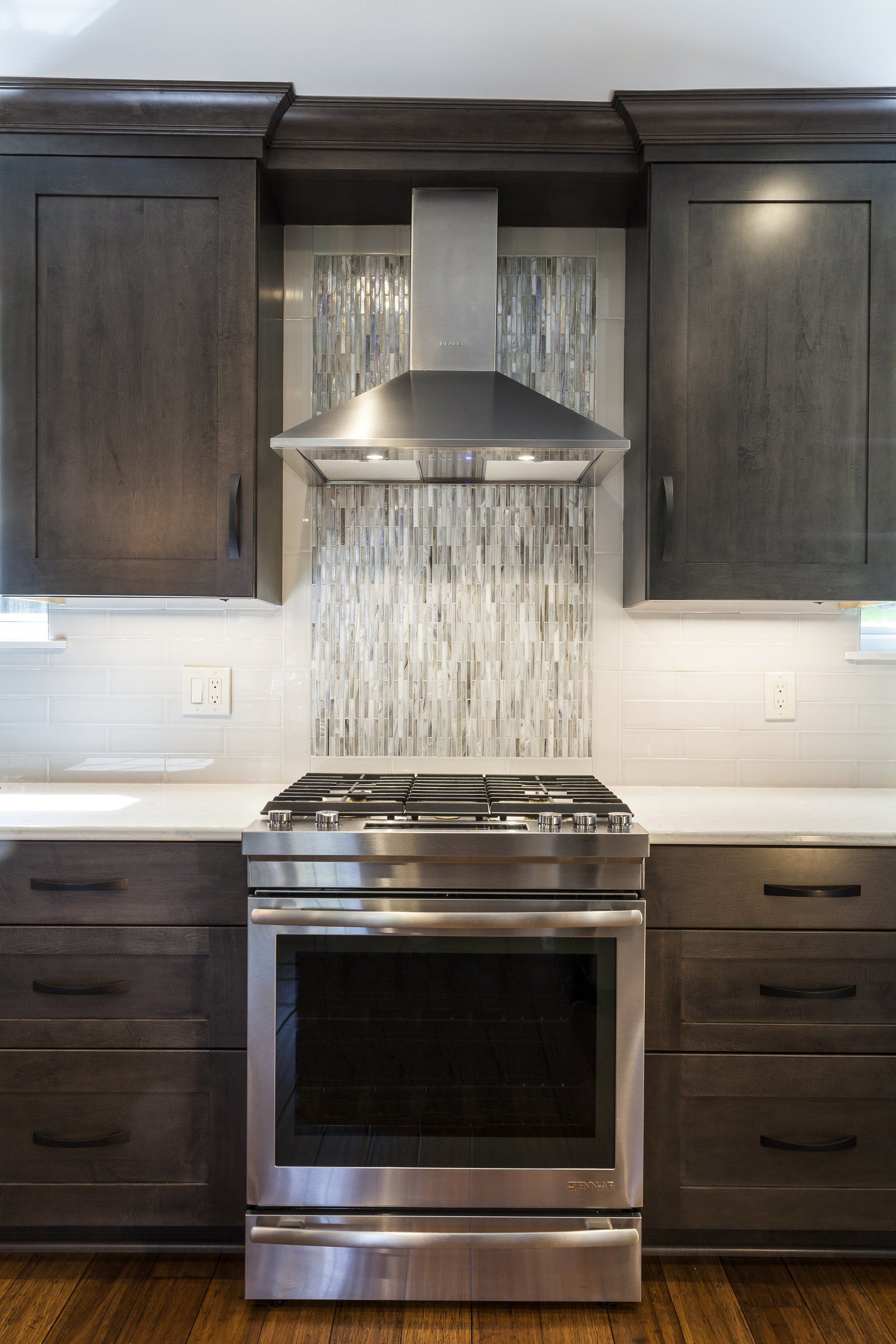 Modern kitchen with dark cabinets, stainless steel range, and range hood centered against a white backsplash