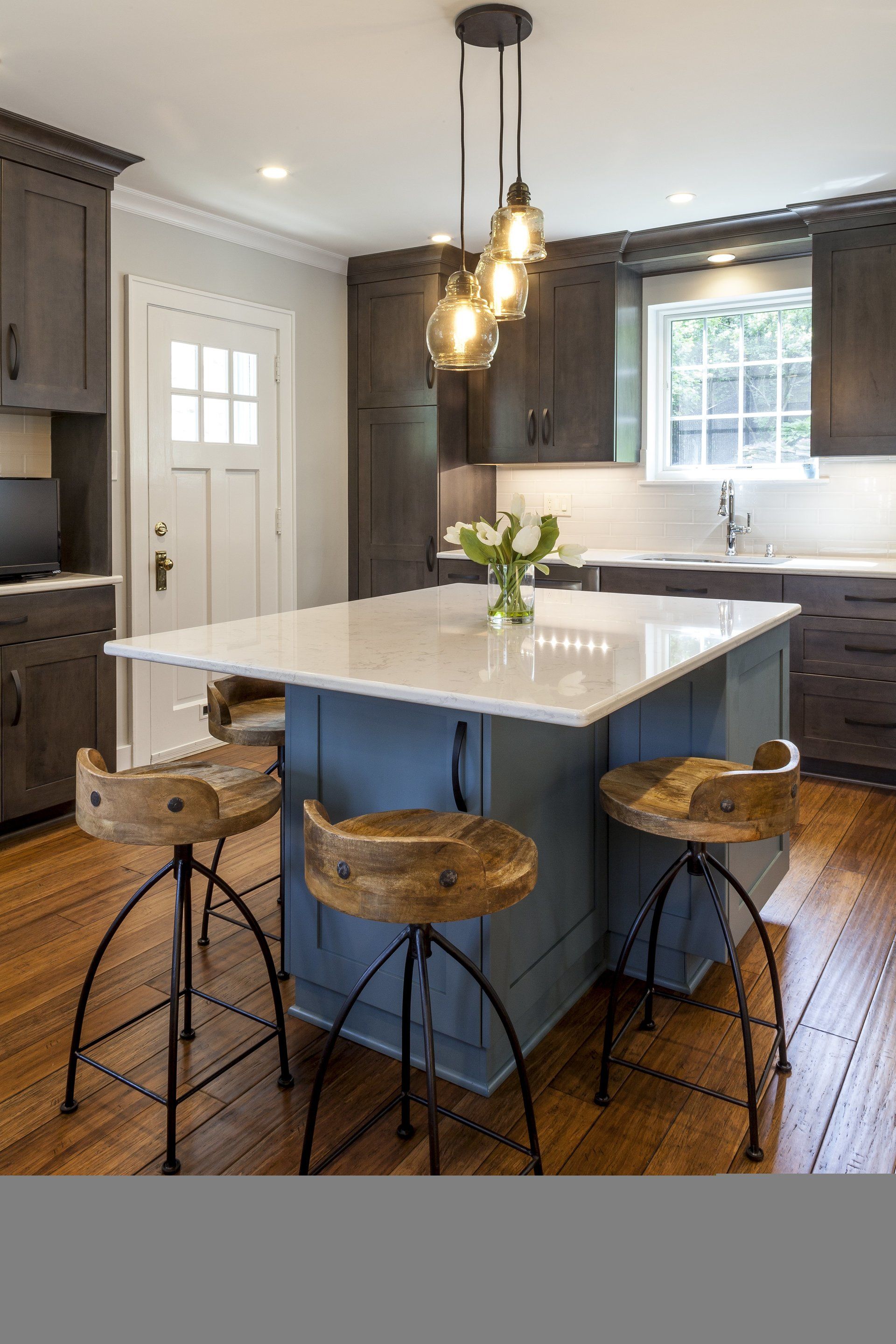 Modern kitchen with navy island, marble countertop, pendant lights, and woven stools