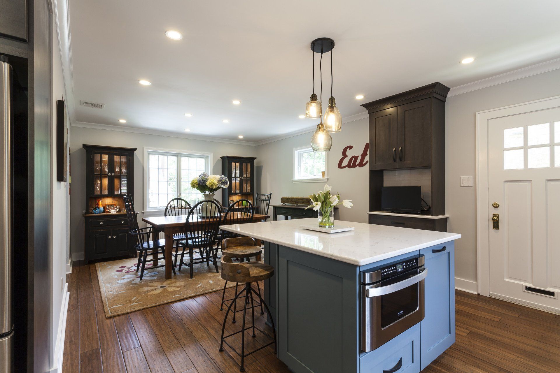 Bright modern kitchen and dining area with island, dark wood floors, white cabinets, and pendant lights