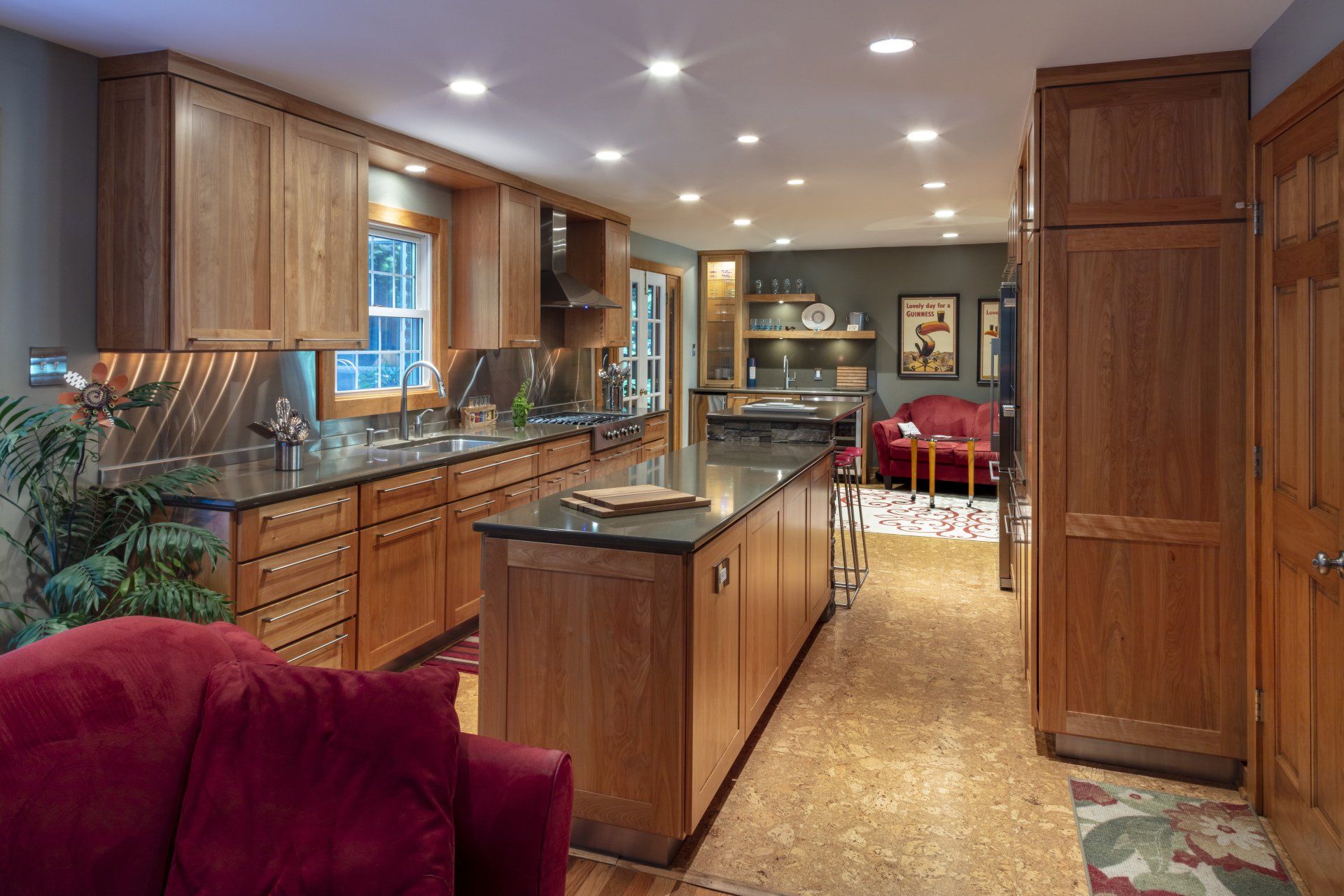 Spacious wood-paneled kitchen with central island, stainless appliances, red chairs, and warm recessed lighting