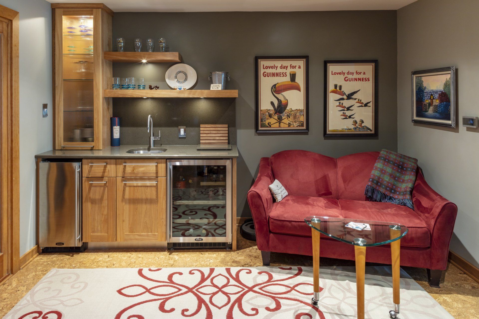 Cozy living room with kitchenette, red loveseat, wall art, and patterned rug