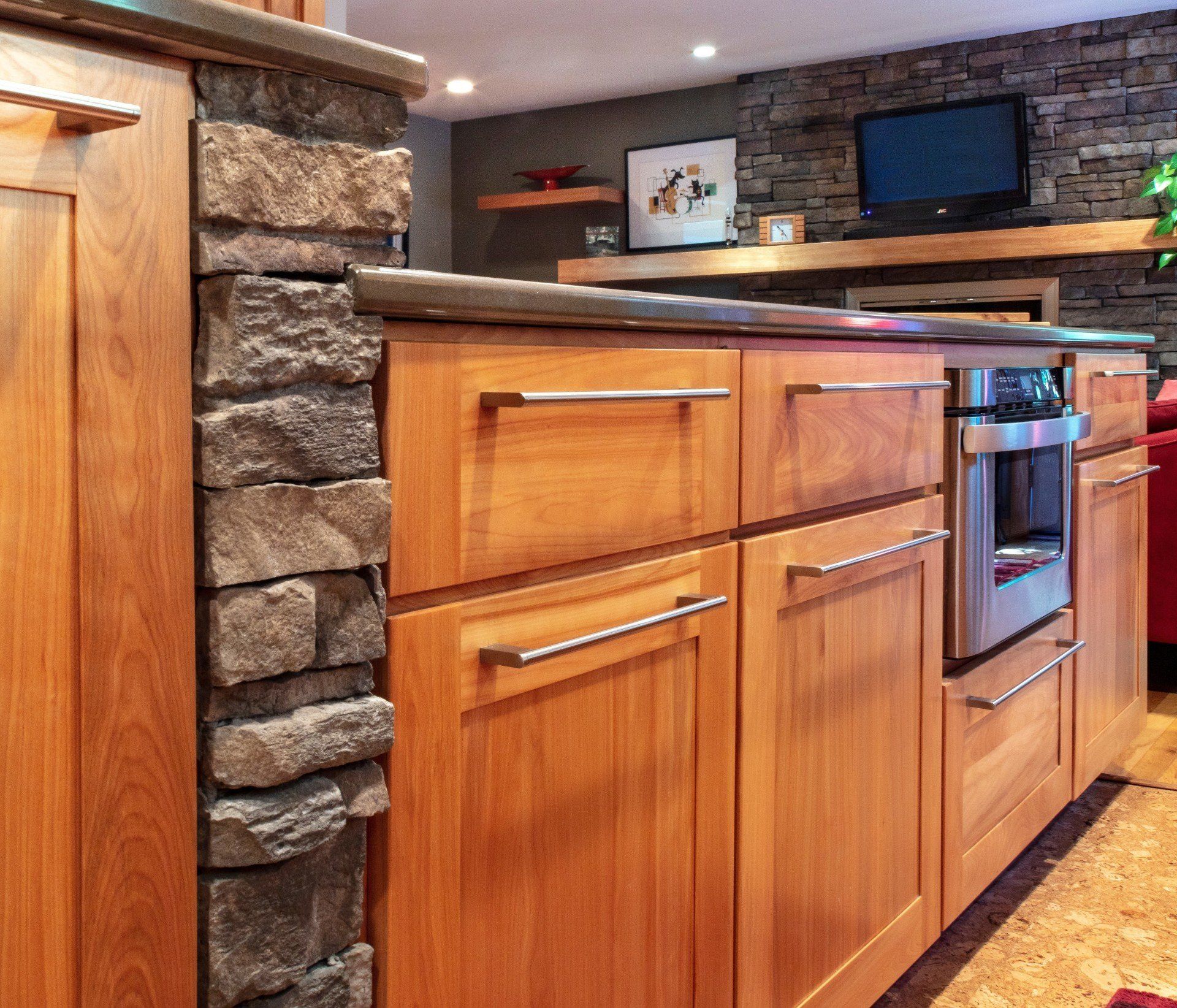 Wood kitchen island with stone accents, wood cabinets, and a built-in oven in a modern rustic kitchen