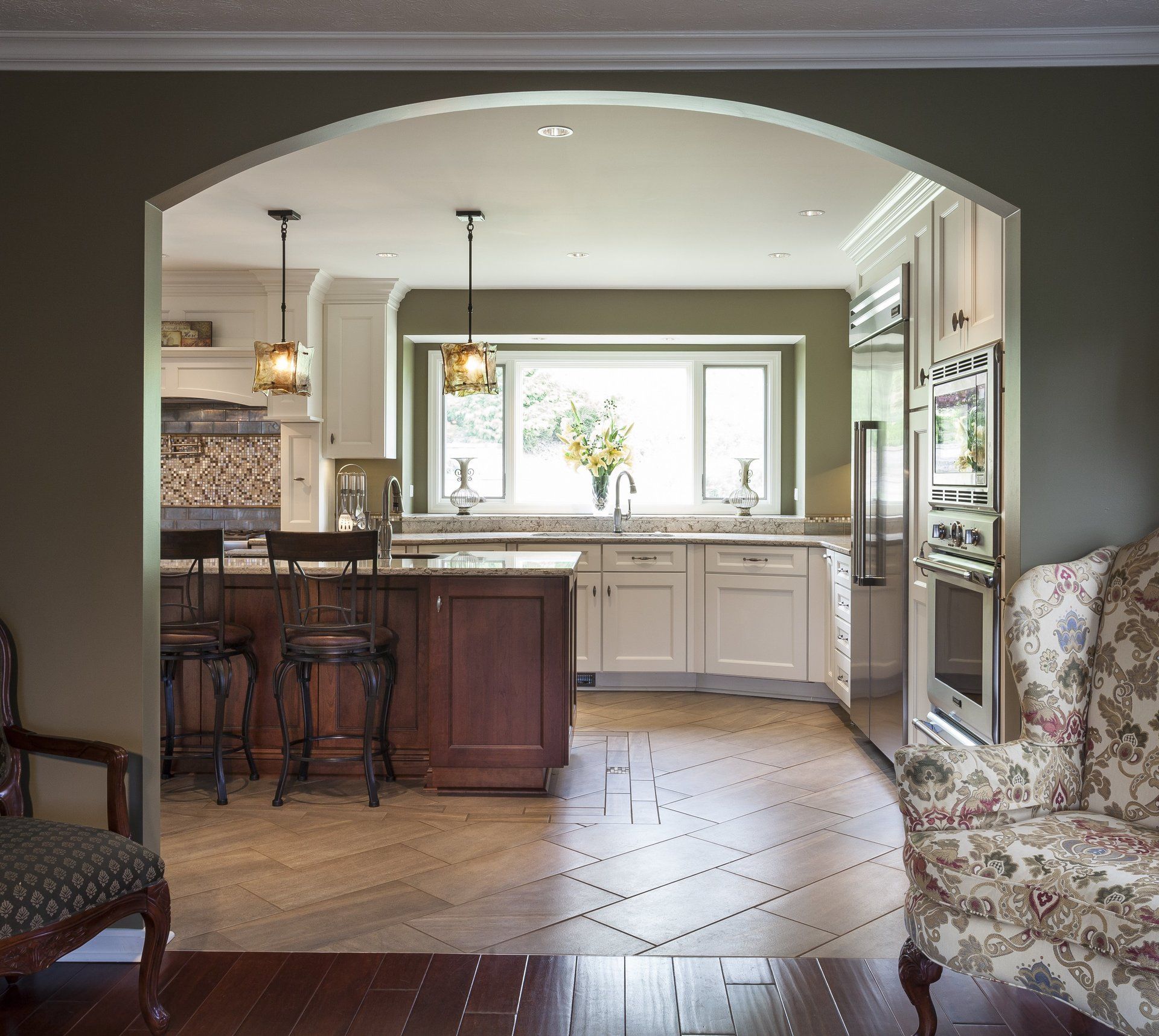 Elegant kitchen with dark island, white cabinets, pendant lights, and floral armchair in foreground
