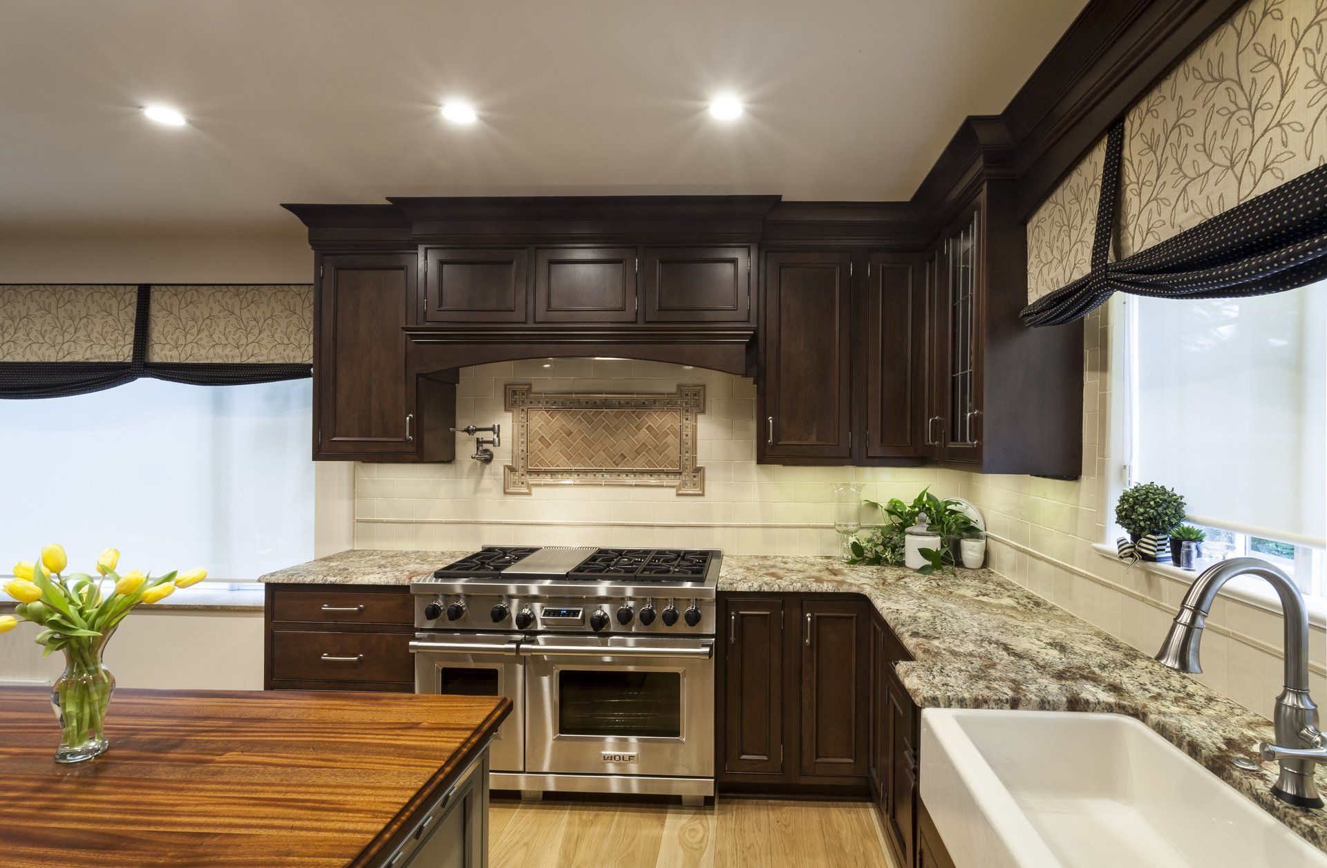 Modern kitchen with dark wood cabinets, stainless steel stove, white sink, and a wooden table with flowers.