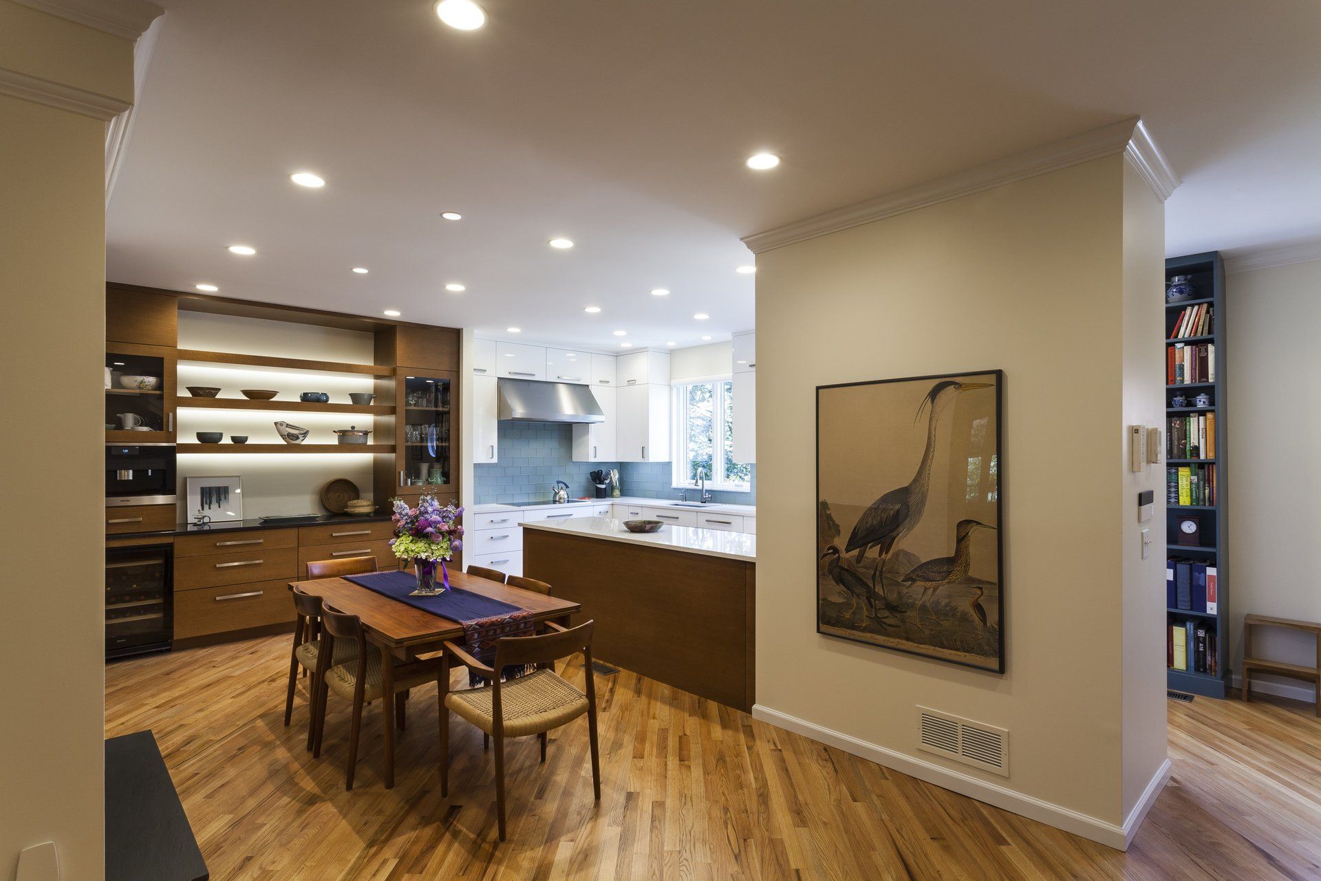 Modern open-plan kitchen and dining area with wooden floors, island counter, and wall art.