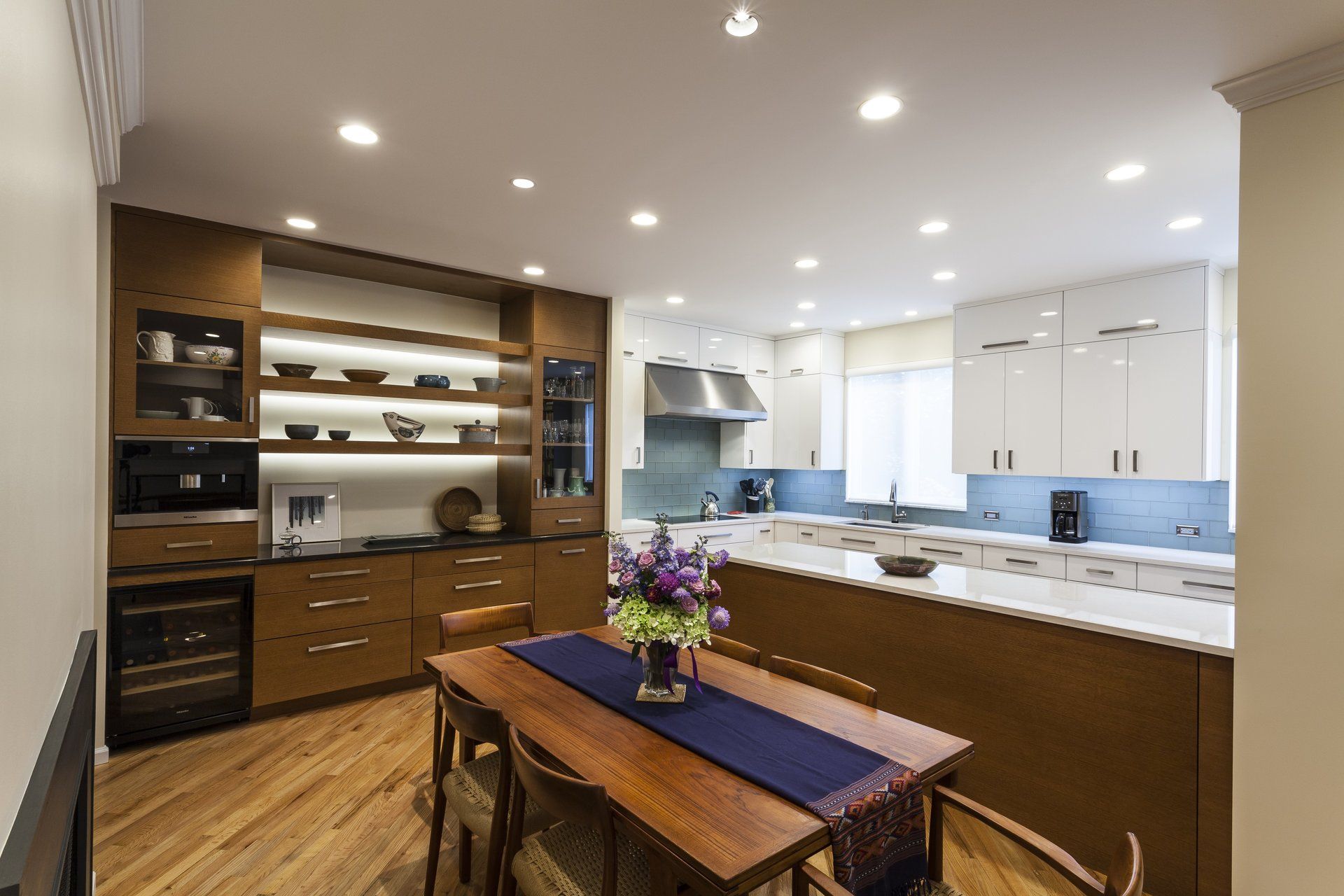 Modern kitchen and dining area with white cabinets, wood accents, and a table with flowers
