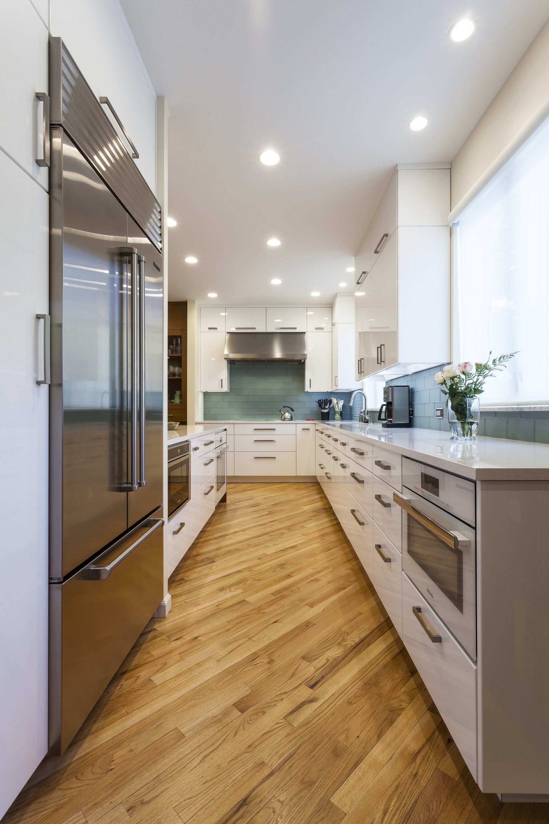 Bright modern galley kitchen with white cabinets, stainless appliances, and wood floors