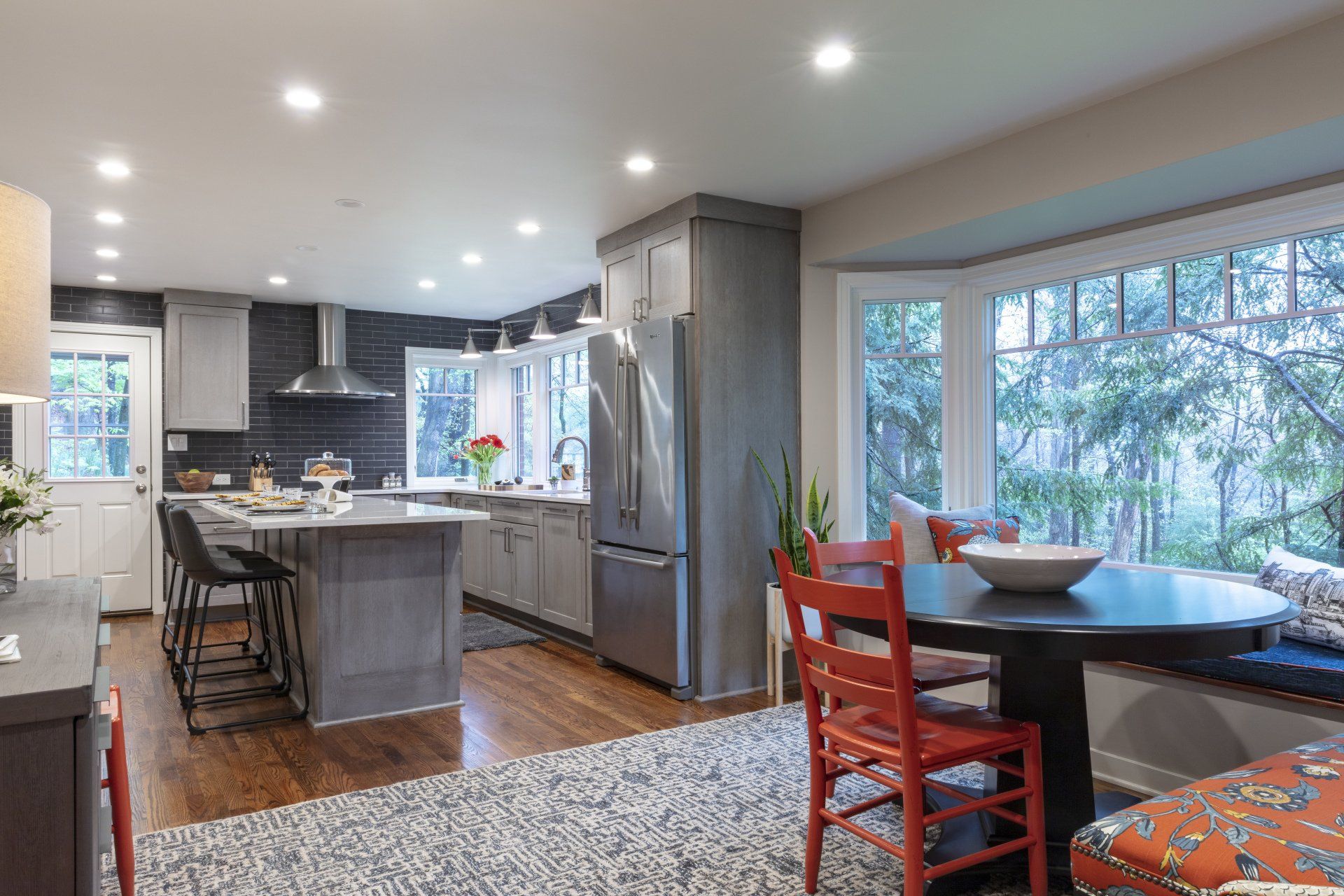 Bright modern kitchen and dining area with island, gray cabinets, wood floors, and a large window view