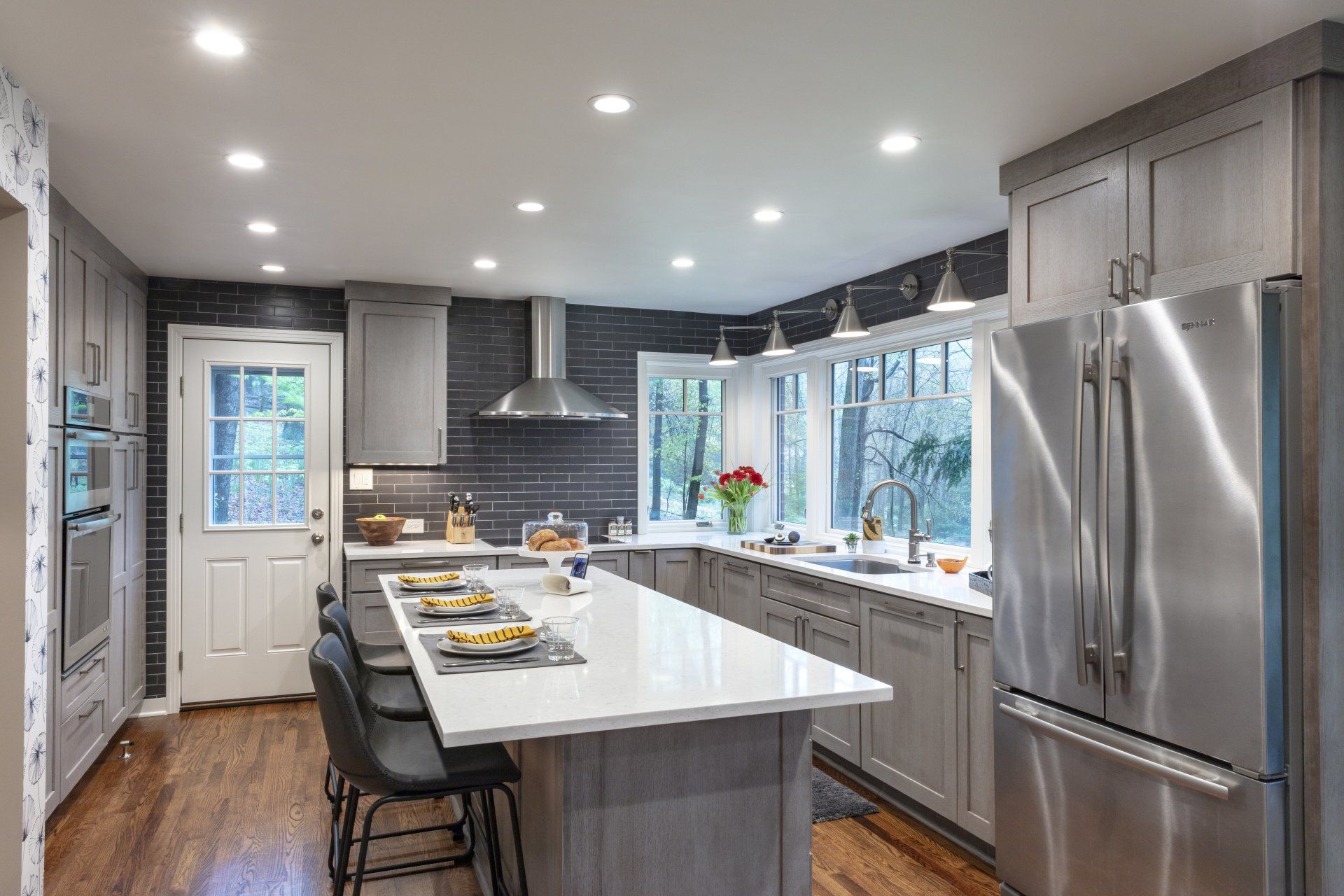 Modern kitchen with gray cabinets, stainless steel appliances, white island, and large bay window