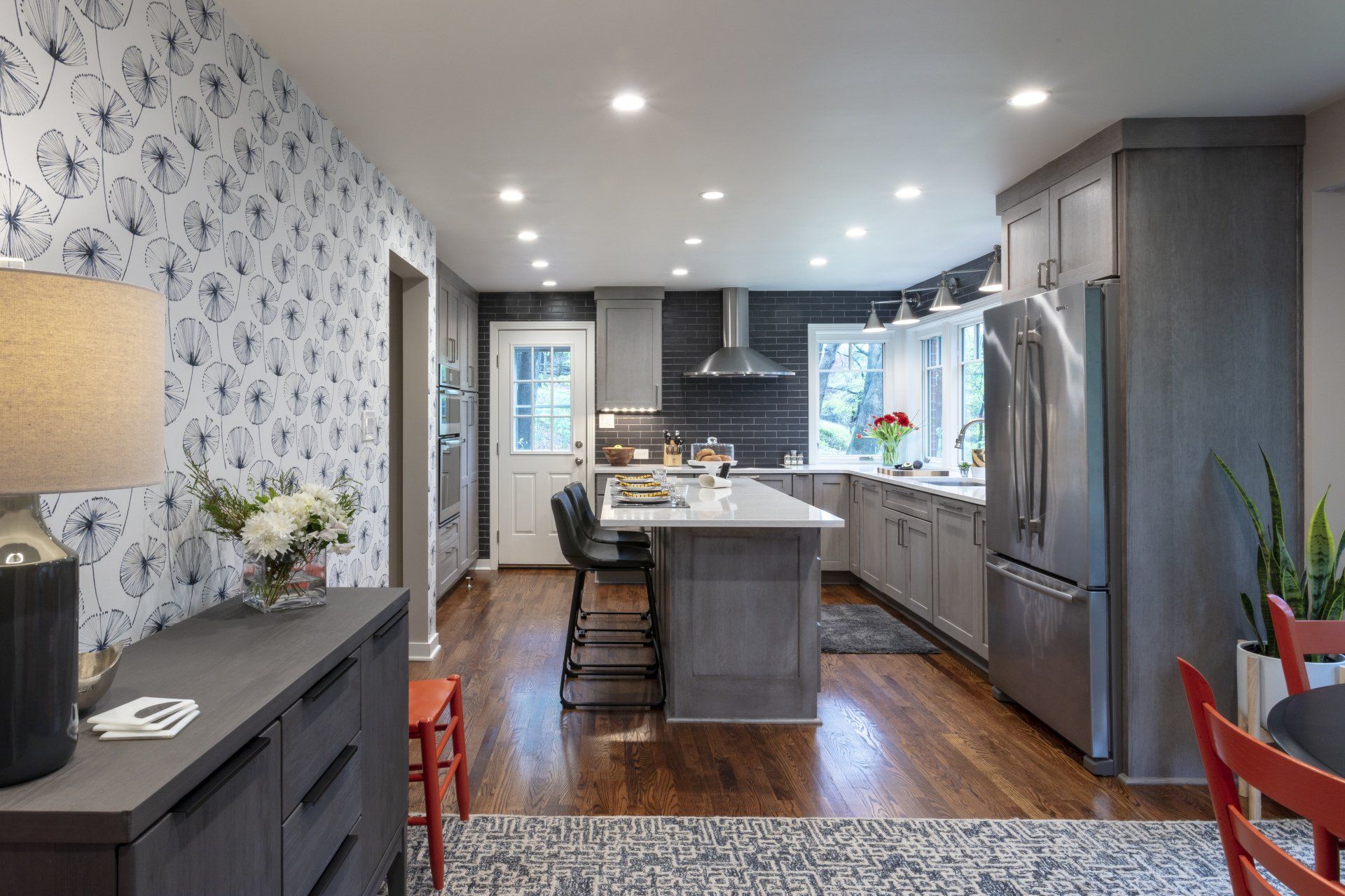 Modern gray kitchen with island, stainless fridge, white countertops, and hardwood floors in bright open space