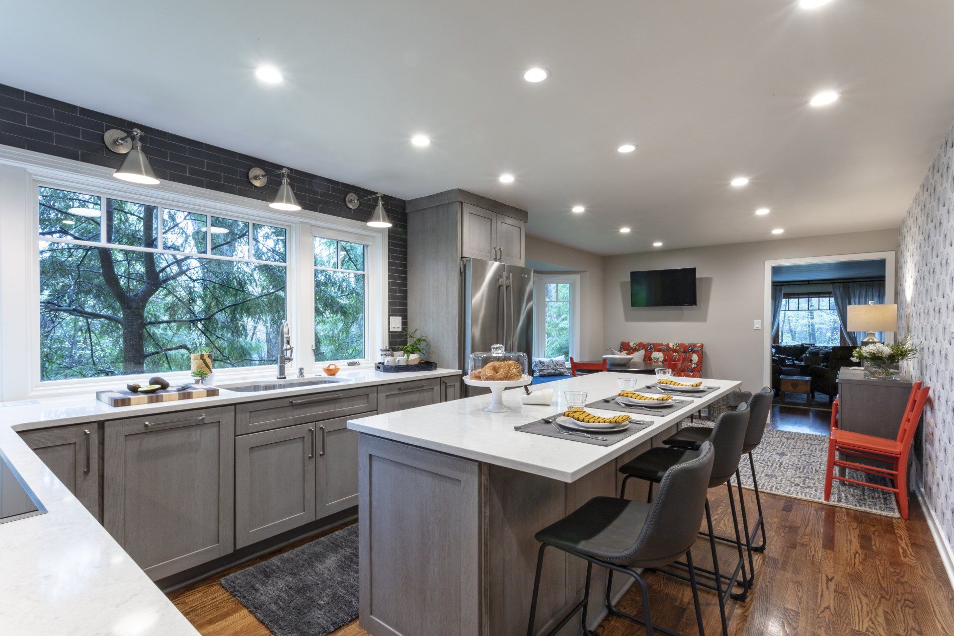Modern kitchen with gray cabinets, white island, black stools, and large windows.
