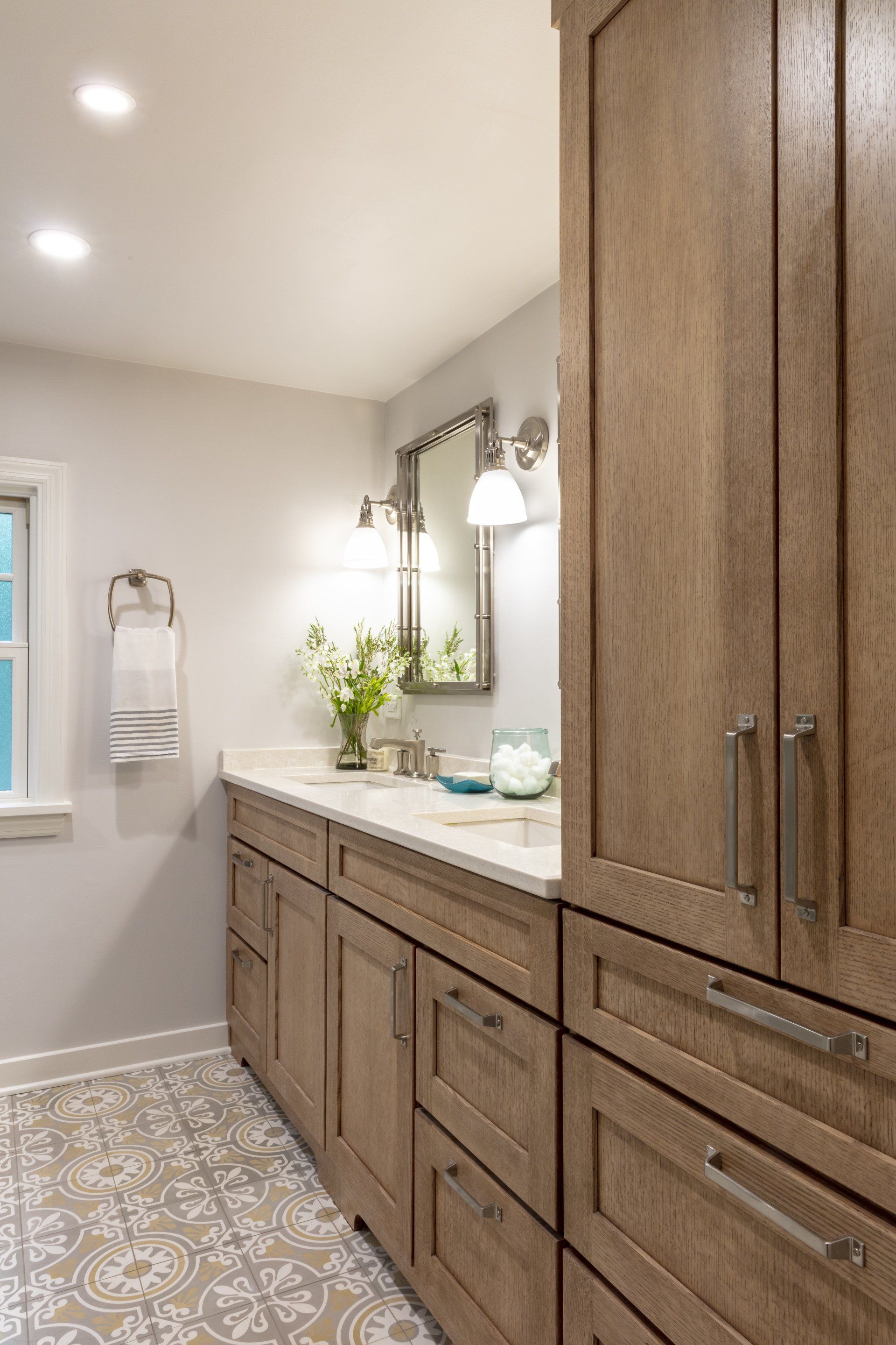 Modern bathroom vanity with wood cabinets, double sinks, patterned tile floor, and mirror lights