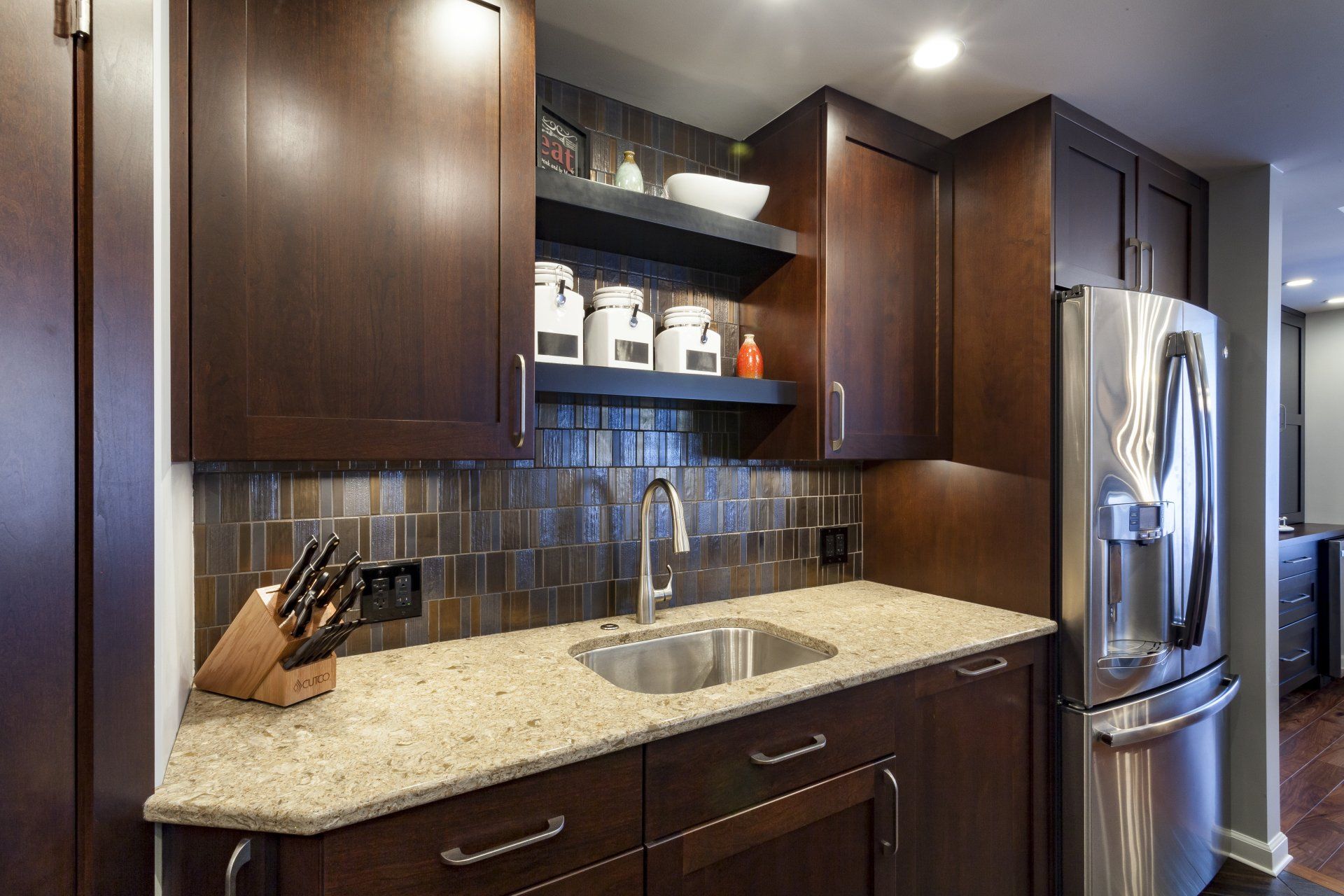 Modern kitchen with dark wood cabinets, granite countertop, tile backsplash, and stainless steel refrigerator
