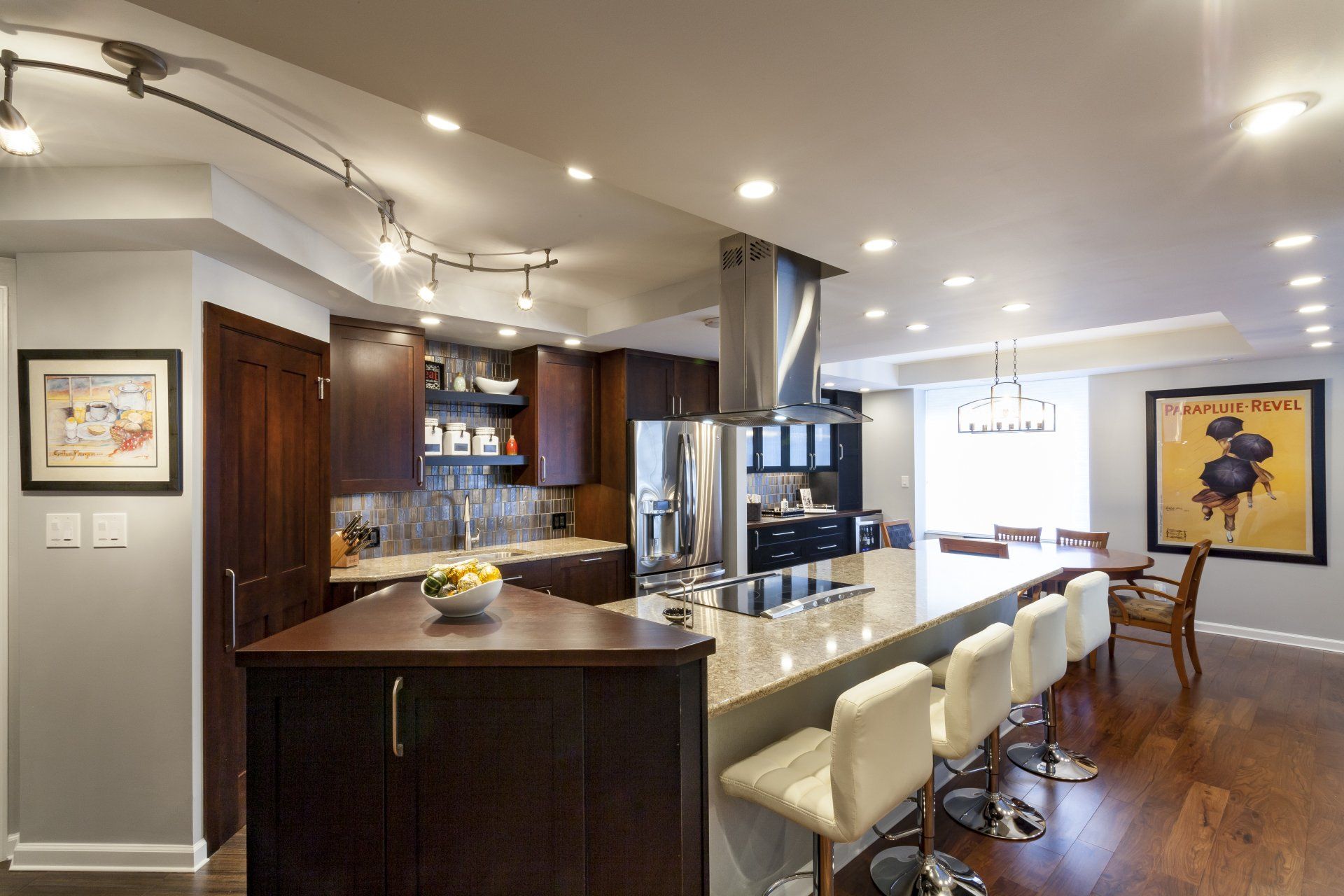 Modern kitchen with dark wood cabinets, white bar stools, and a breakfast island under pendant lights