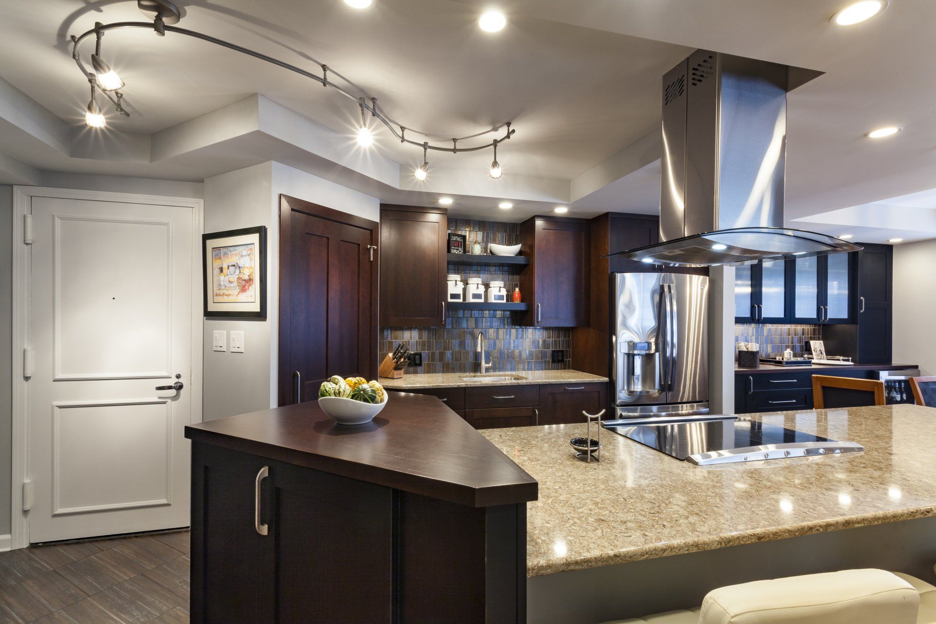 Modern kitchen with granite island, stainless steel appliances, dark cabinets, and track lighting