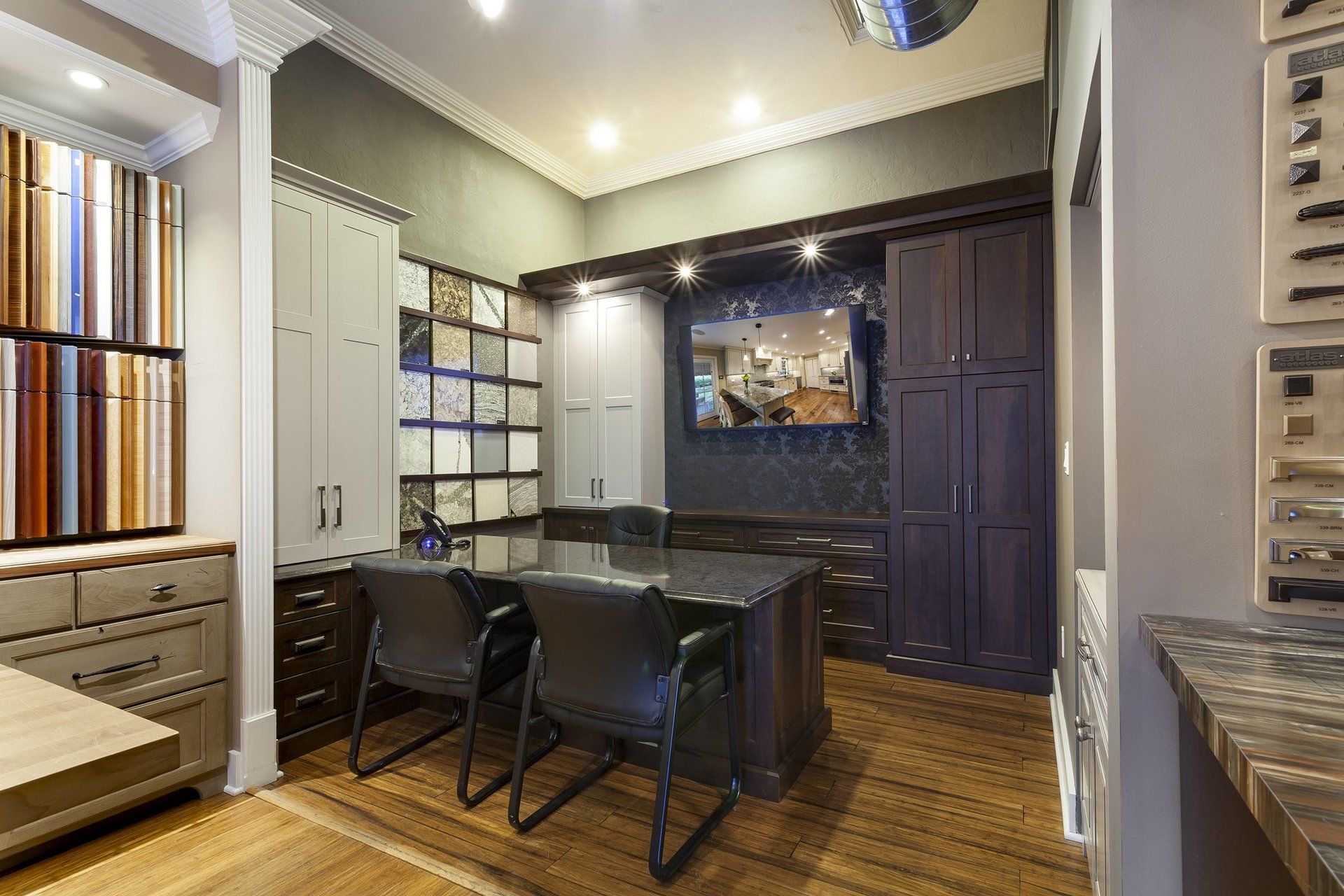 Modern office with dark desk, black chairs, built-in shelves, and a wall-mounted TV on wood flooring.