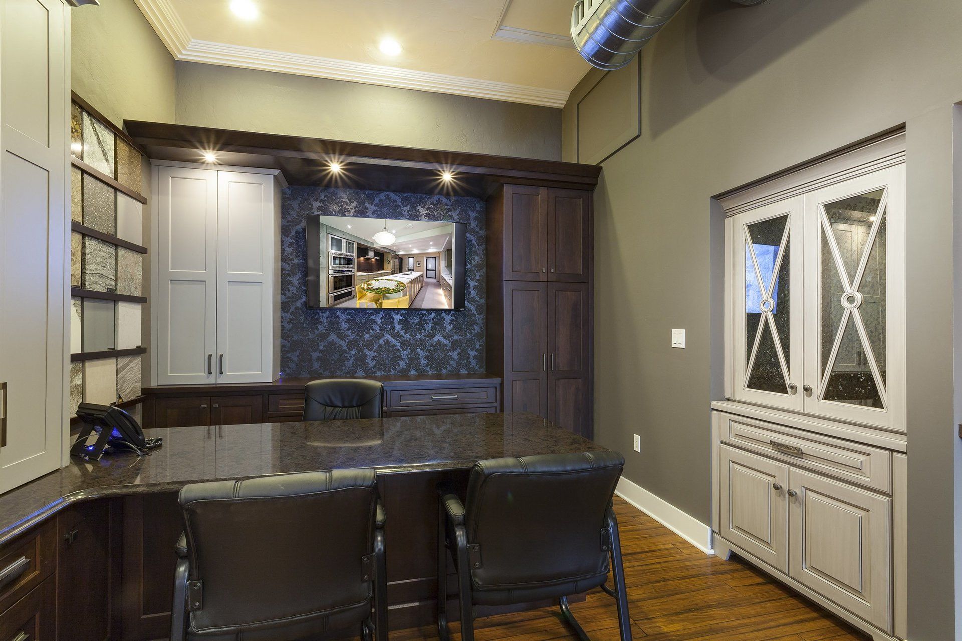 Home office nook with dark wood desk, built-in cabinets, and a pair of black chairs under warm lighting