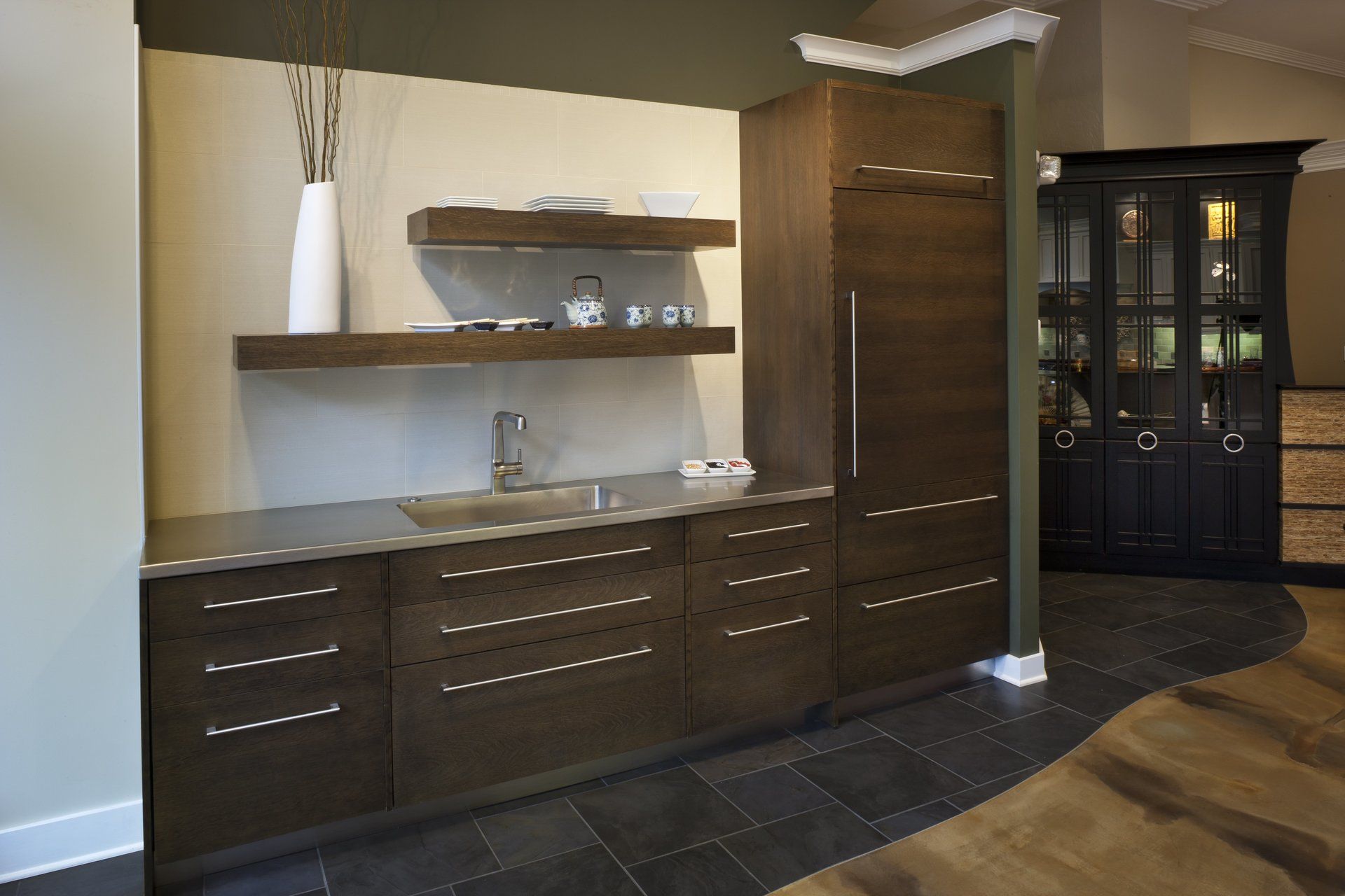 Modern kitchenette with dark wood cabinets, open shelves, and a black display cabinet in a warm-toned room