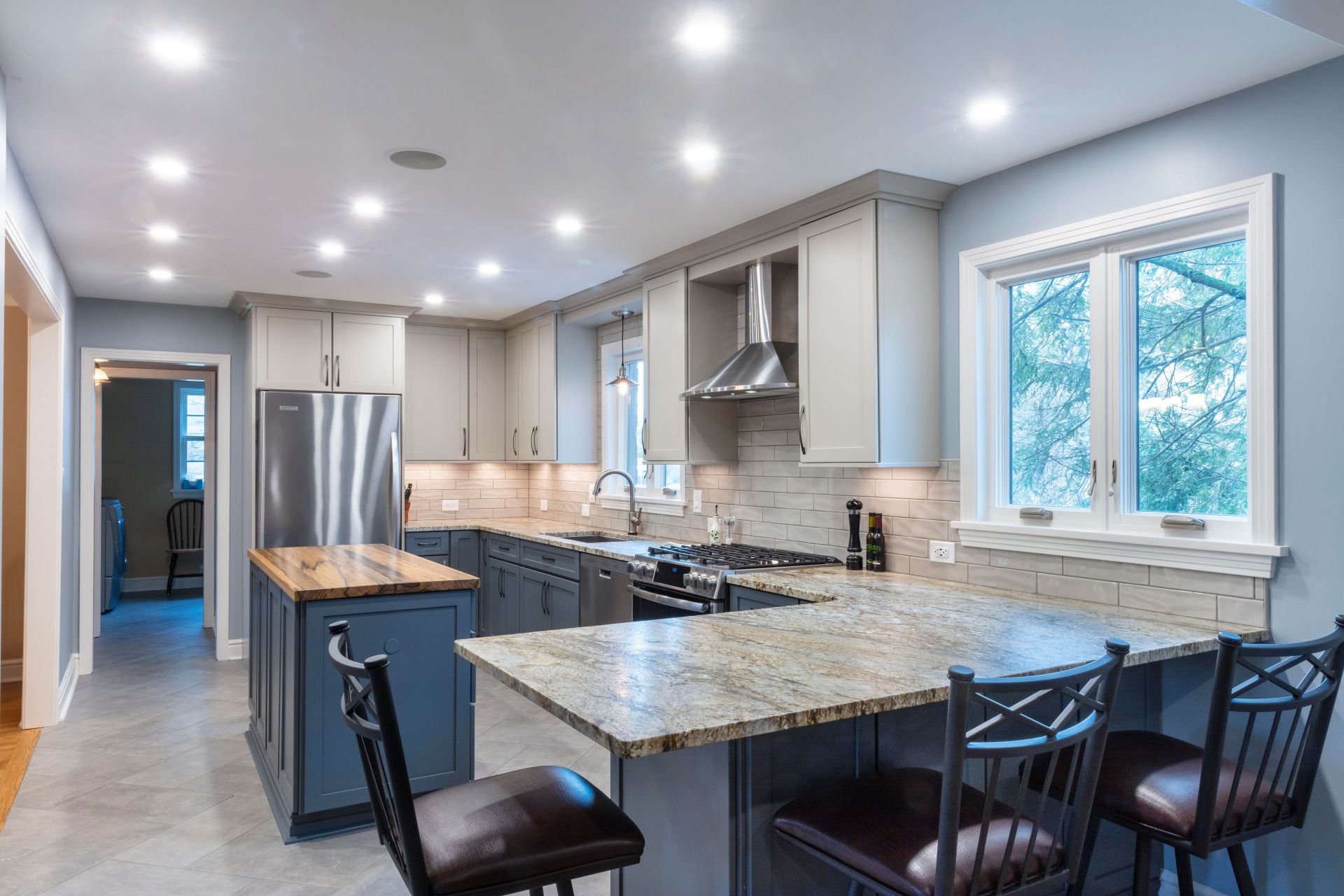 Modern kitchen with granite island, stainless appliances, white cabinets, and black bar stools
